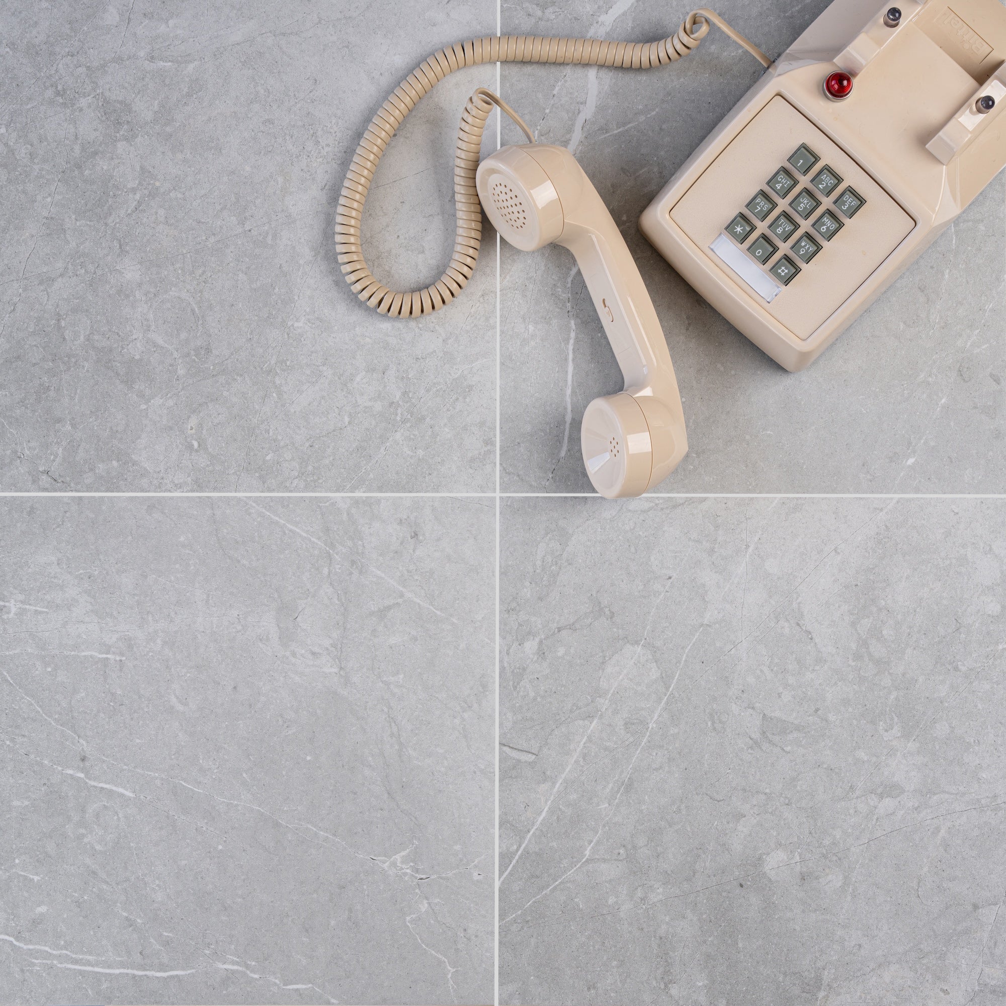 Beige rotary phone handset placed on large grey porcelain tiles with subtle veining and clean grout lines