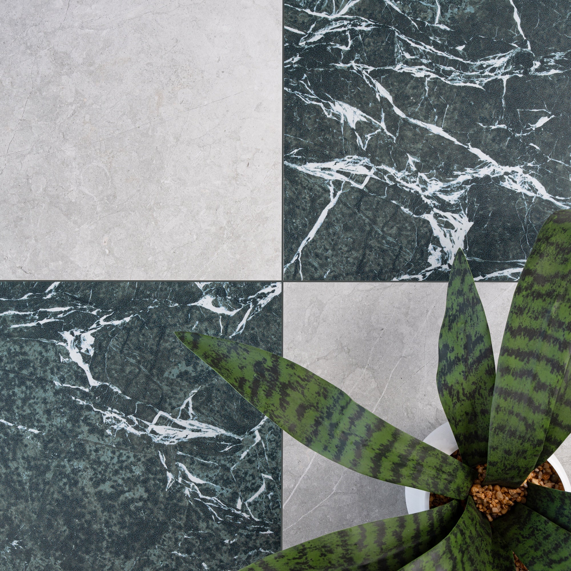 Large square tiles alternating dark green marble with white veining and light gray stone-look surfaces beside a green potted plant