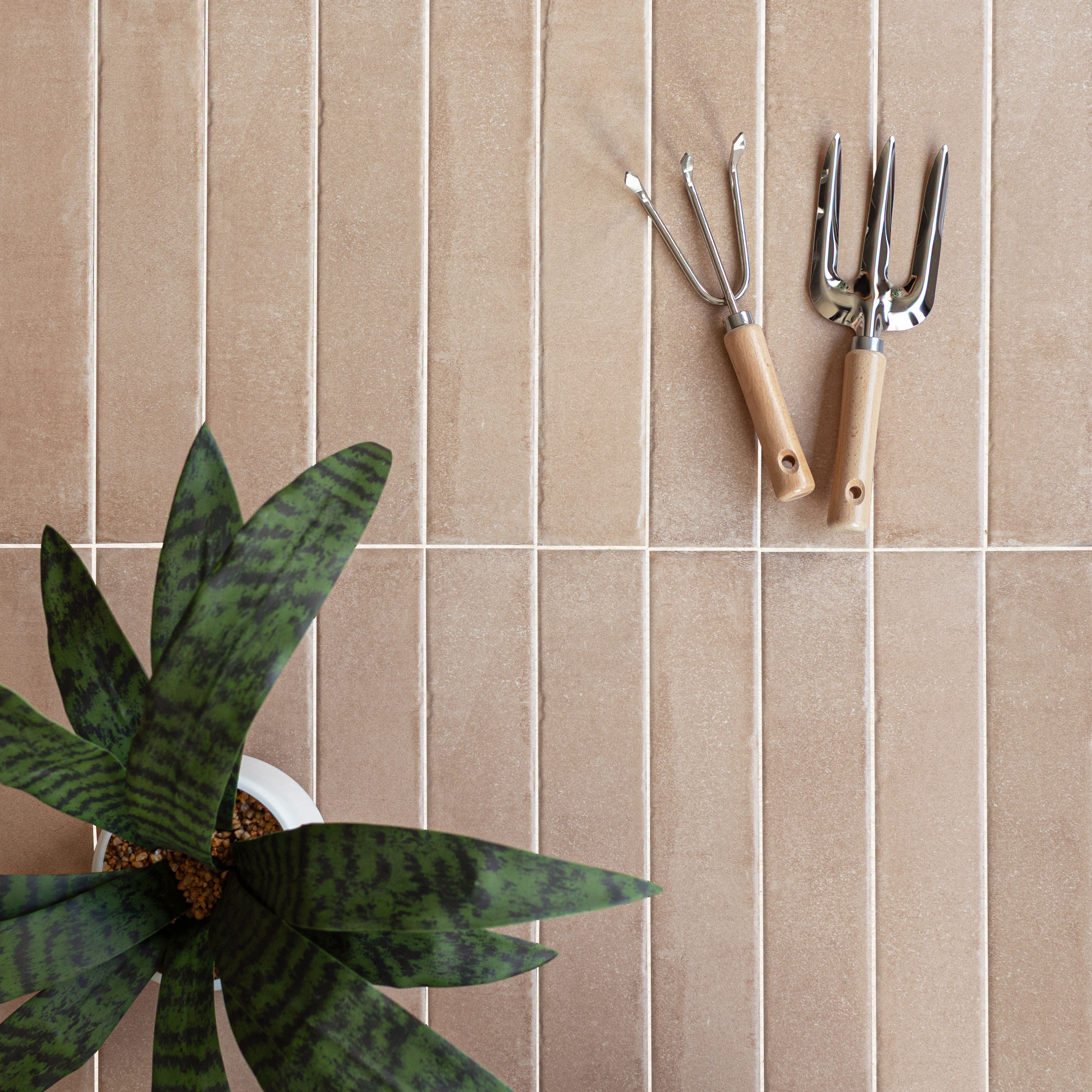Rows of narrow beige ceramic tiles with gardening tools and a green potted plant on the side