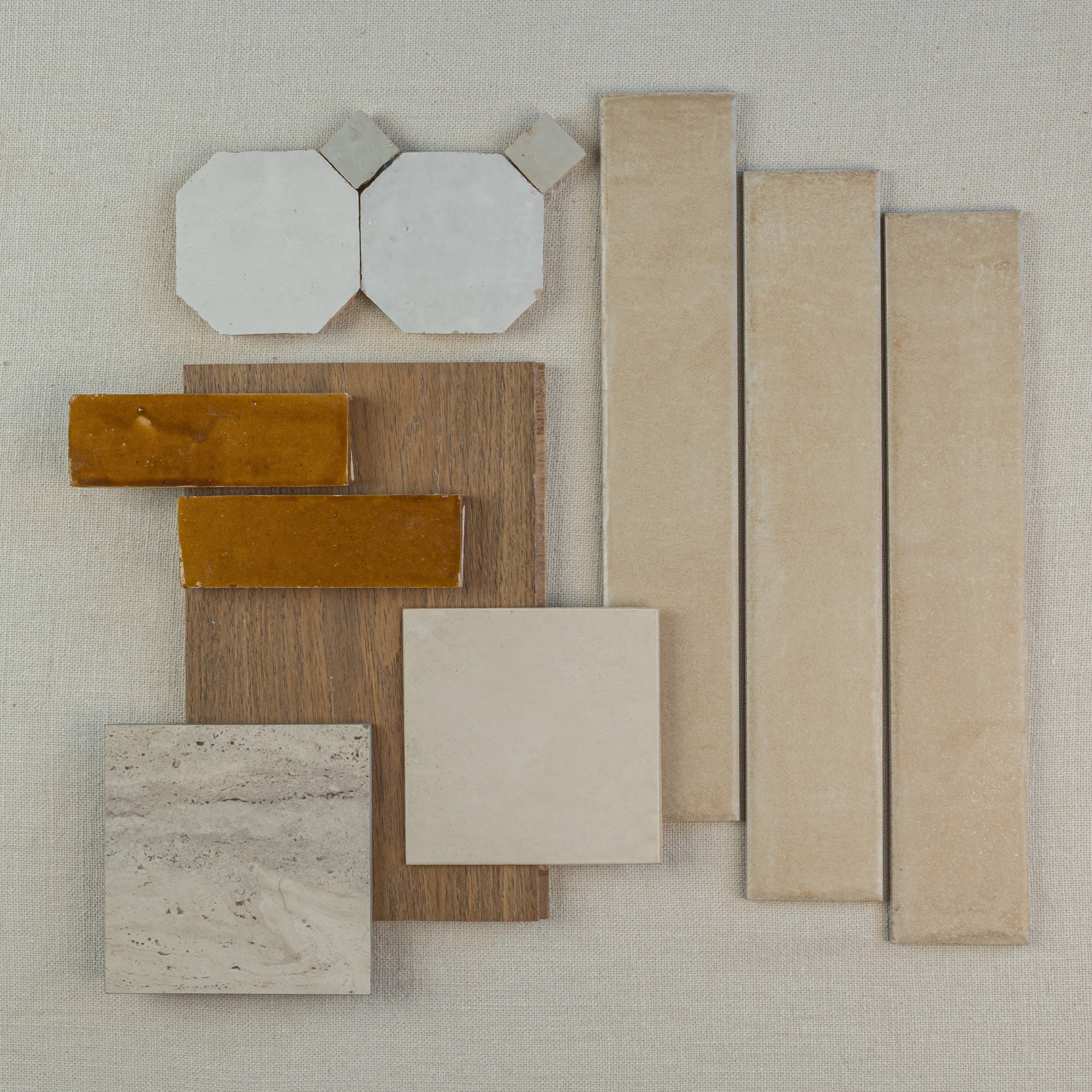 Flat lay of beige rectangular and square tiles, hexagonal ceramic pieces, amber ceramic tiles, and a wood sample on fabric background