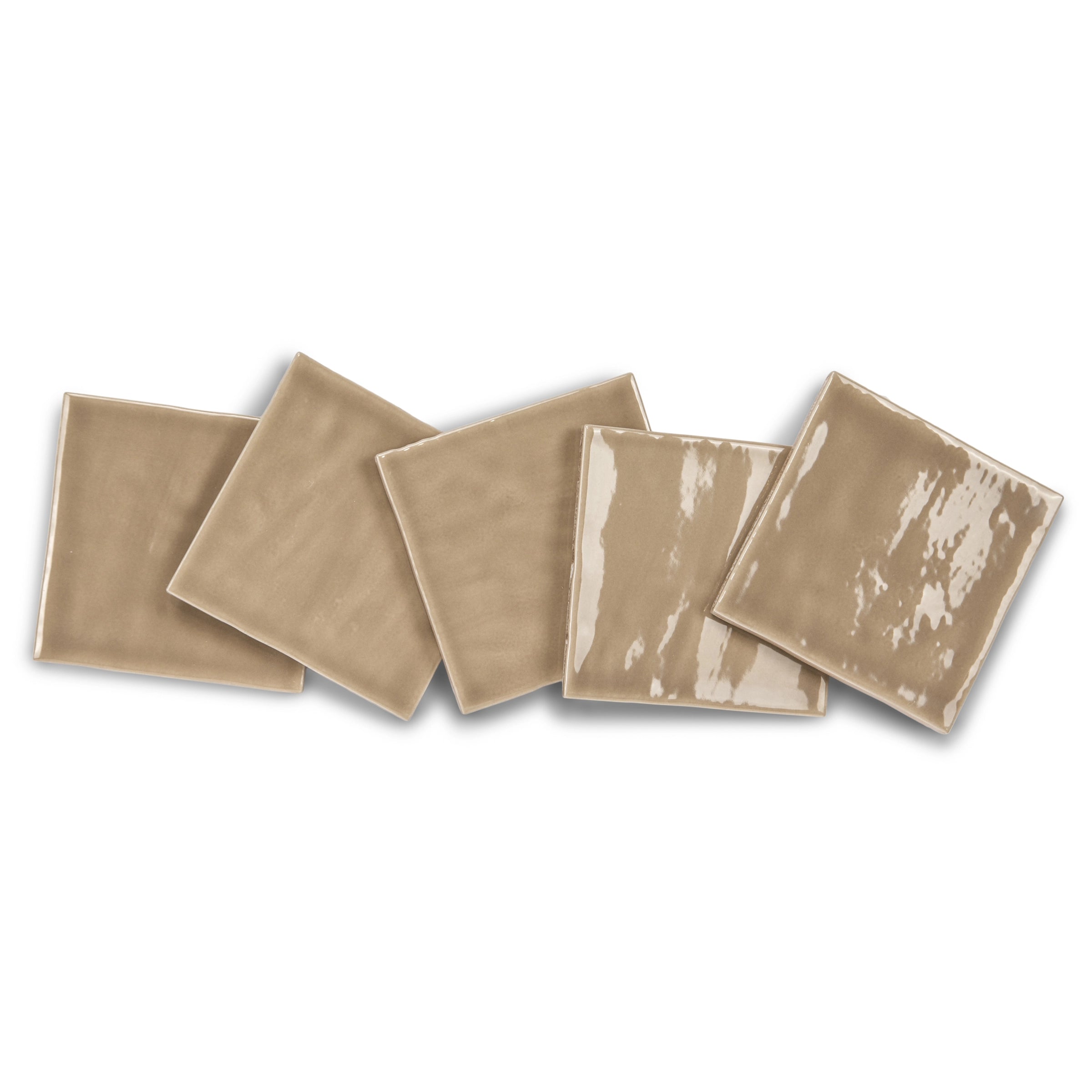 Glossy square ceramic tiles in warm sand tones with slight variations in texture arranged in a scattered line