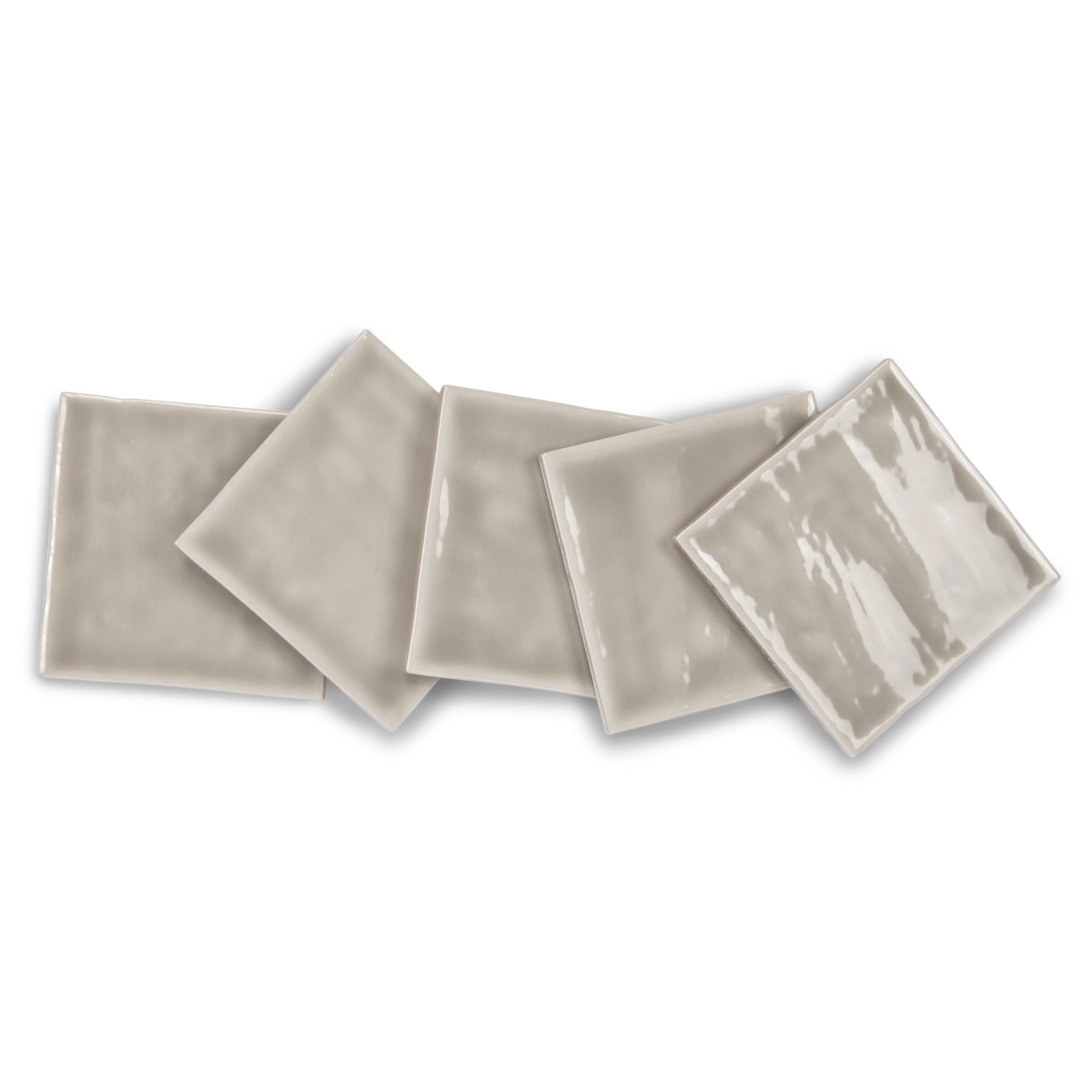 Set of glossy light gray ceramic tiles with subtle surface irregularities arranged loosely on a white background