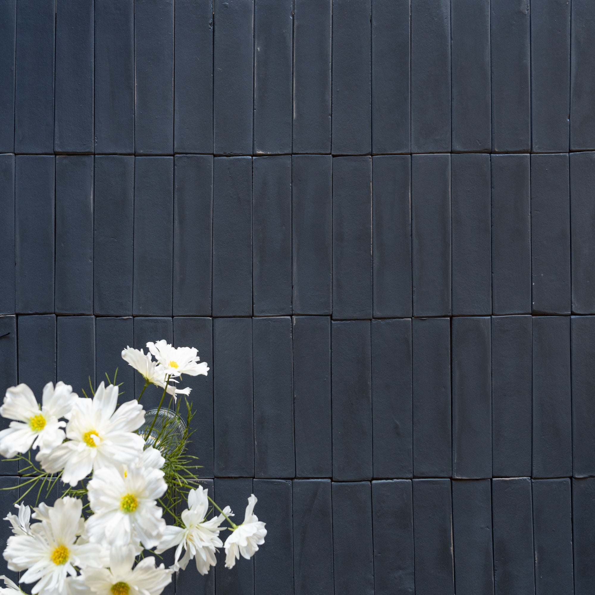 Matte navy rectangular ceramic tiles arranged in a grid pattern with white daisies in the lower left corner