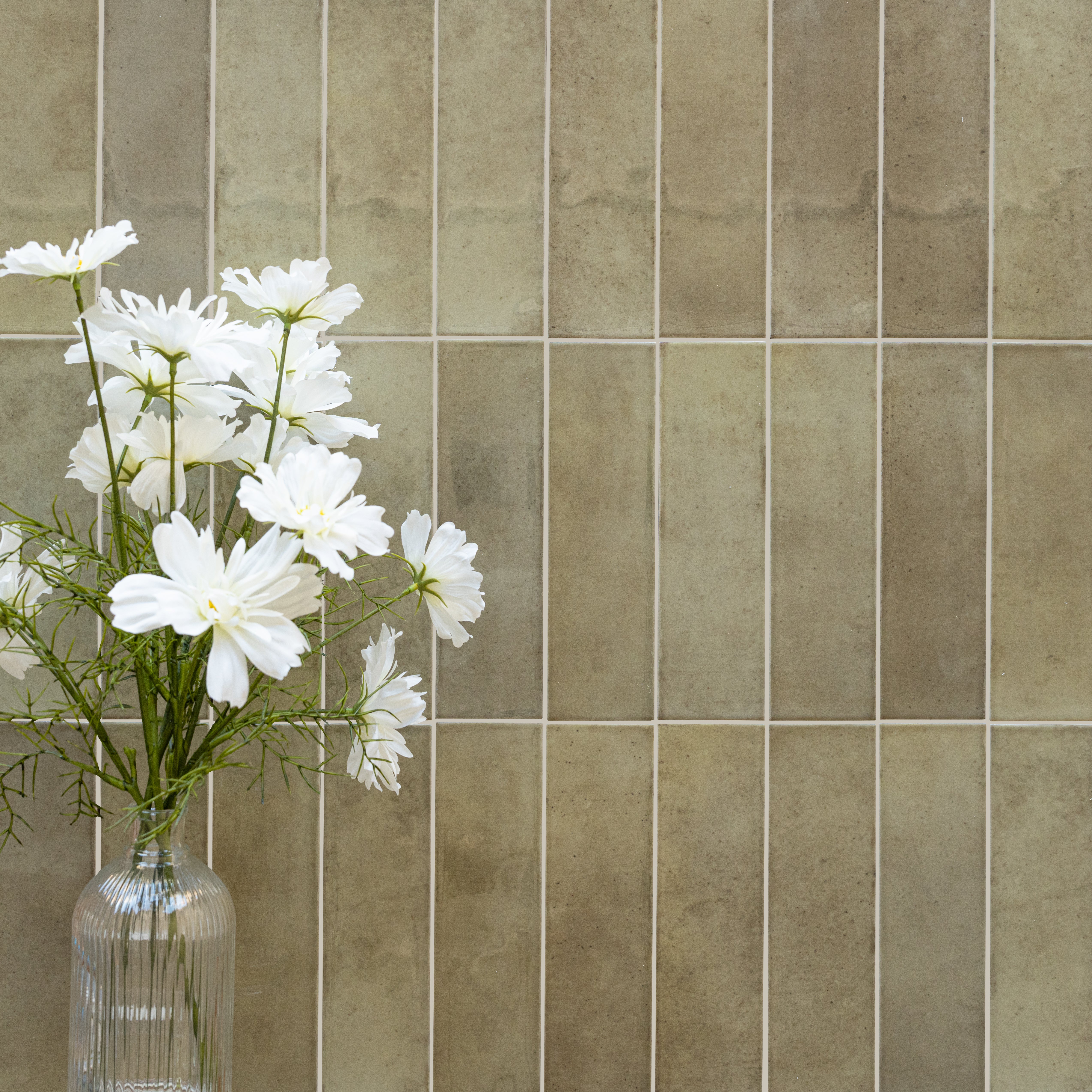 Tall rectangular ceramic tiles in warm muted beige with a matte finish and white daisies in a glass vase nearby