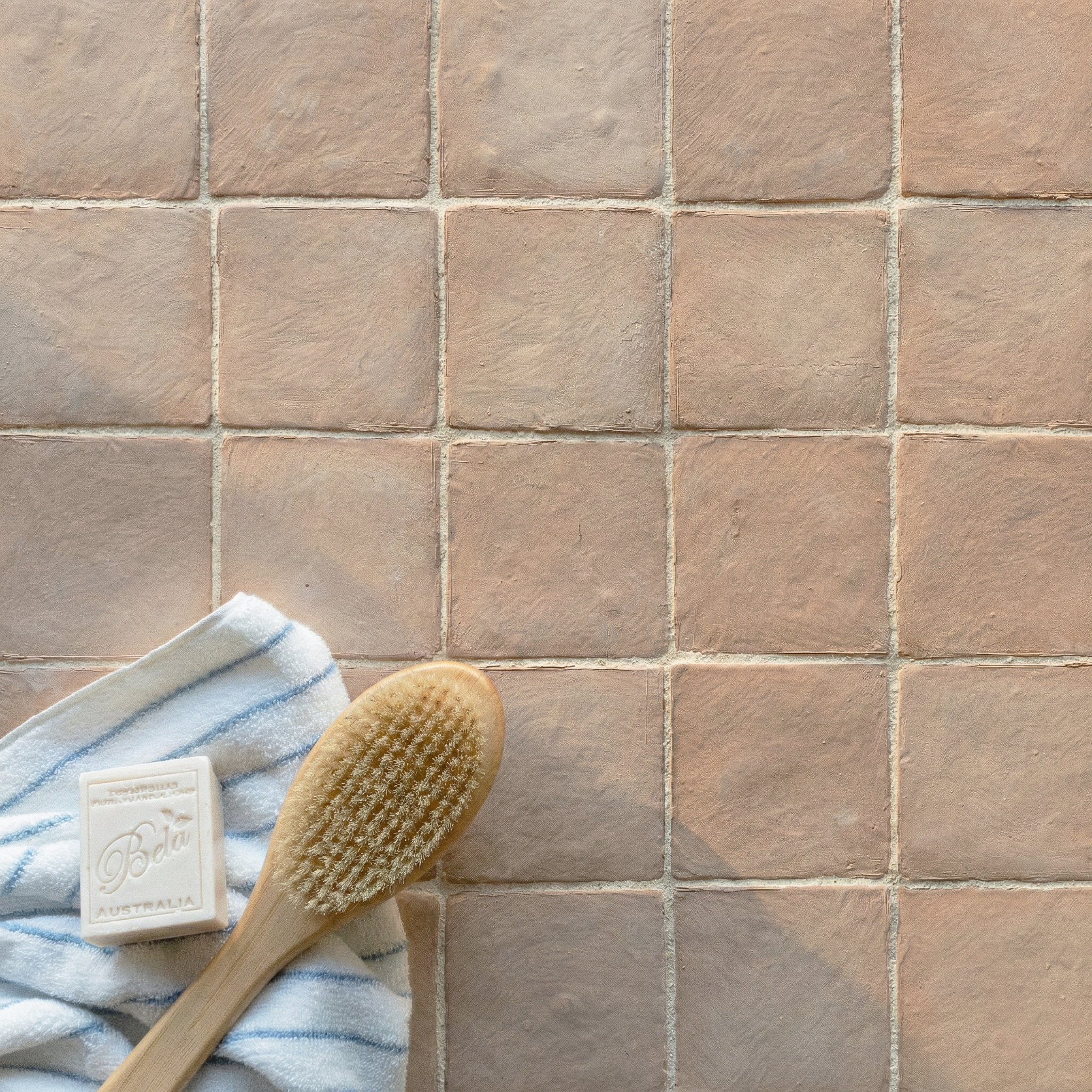 Beige ceramic tiles with a subtle matte texture arranged in a grid beside a wooden brush, soap, and striped cloth