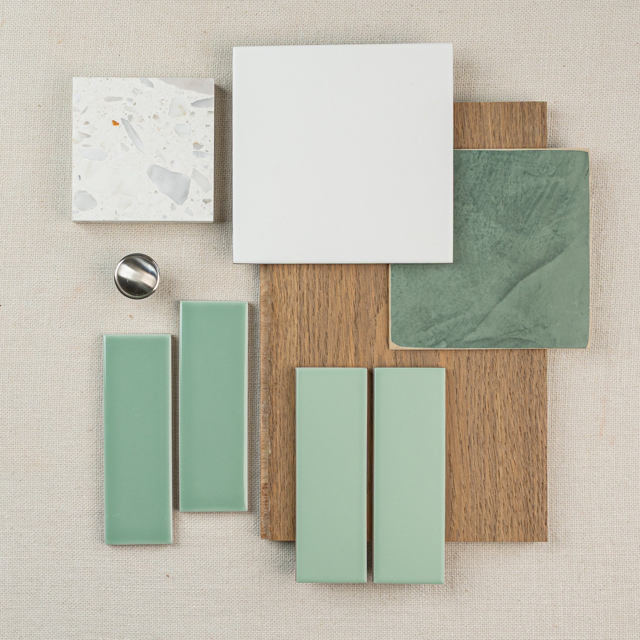Flat lay of green ceramic tiles, white large and terrazzo tiles, wood samples, and a metal ring on fabric background
