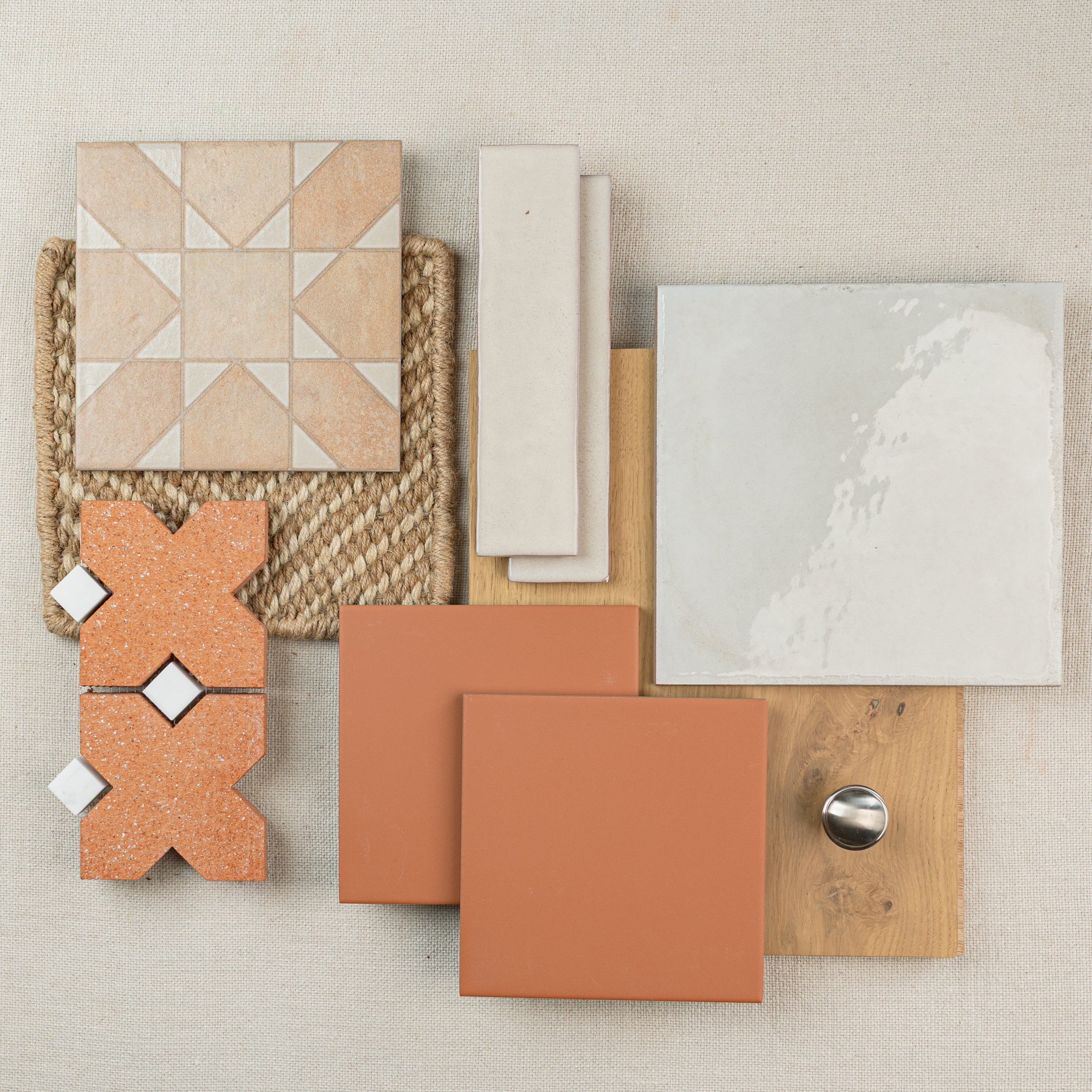 Flat lay of assorted ceramic and terracotta tiles, engineered wood sample, and a metal knob on neutral fabric background