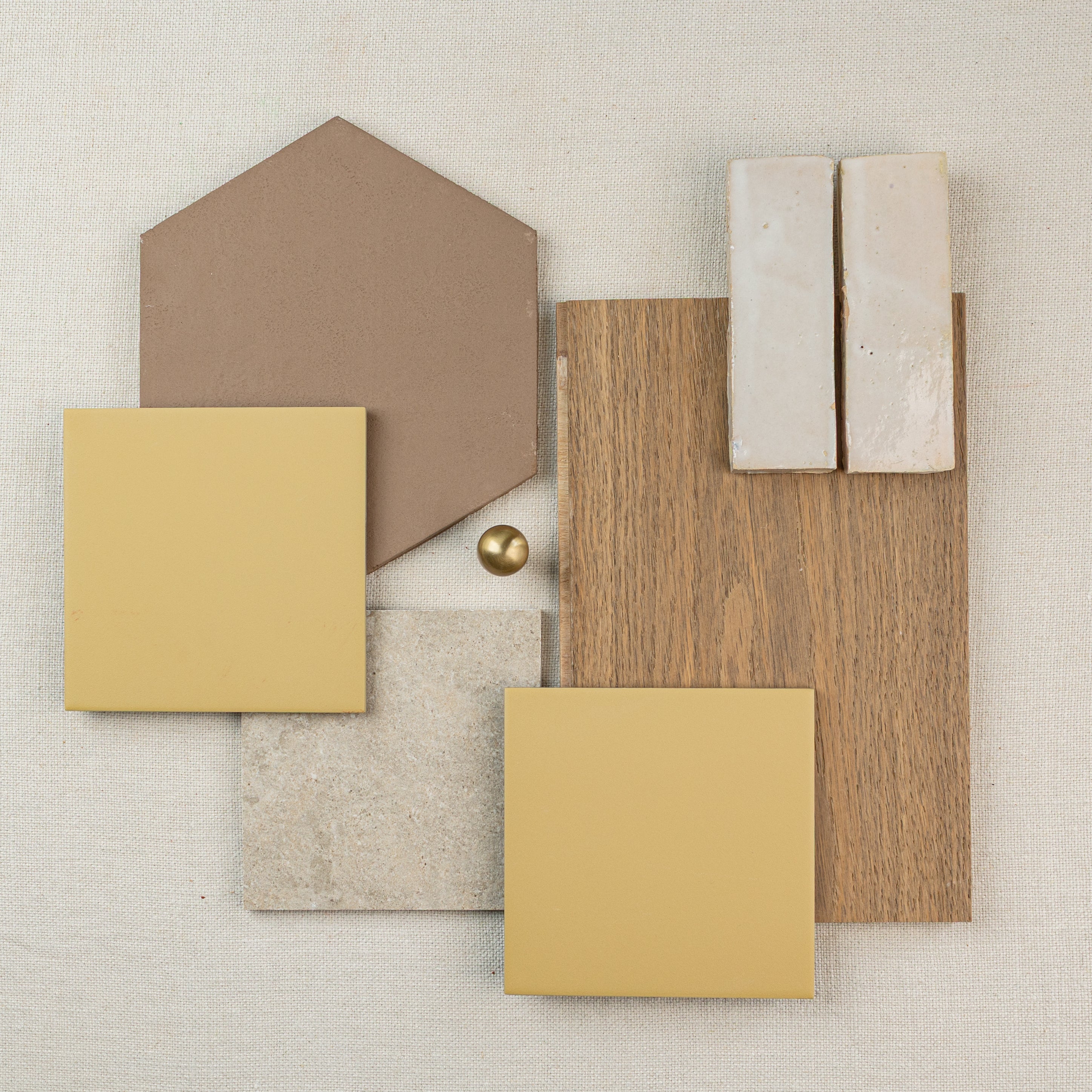 Flat lay of earth-toned tile and wood samples arranged on fabric background with gold accents for design inspiration