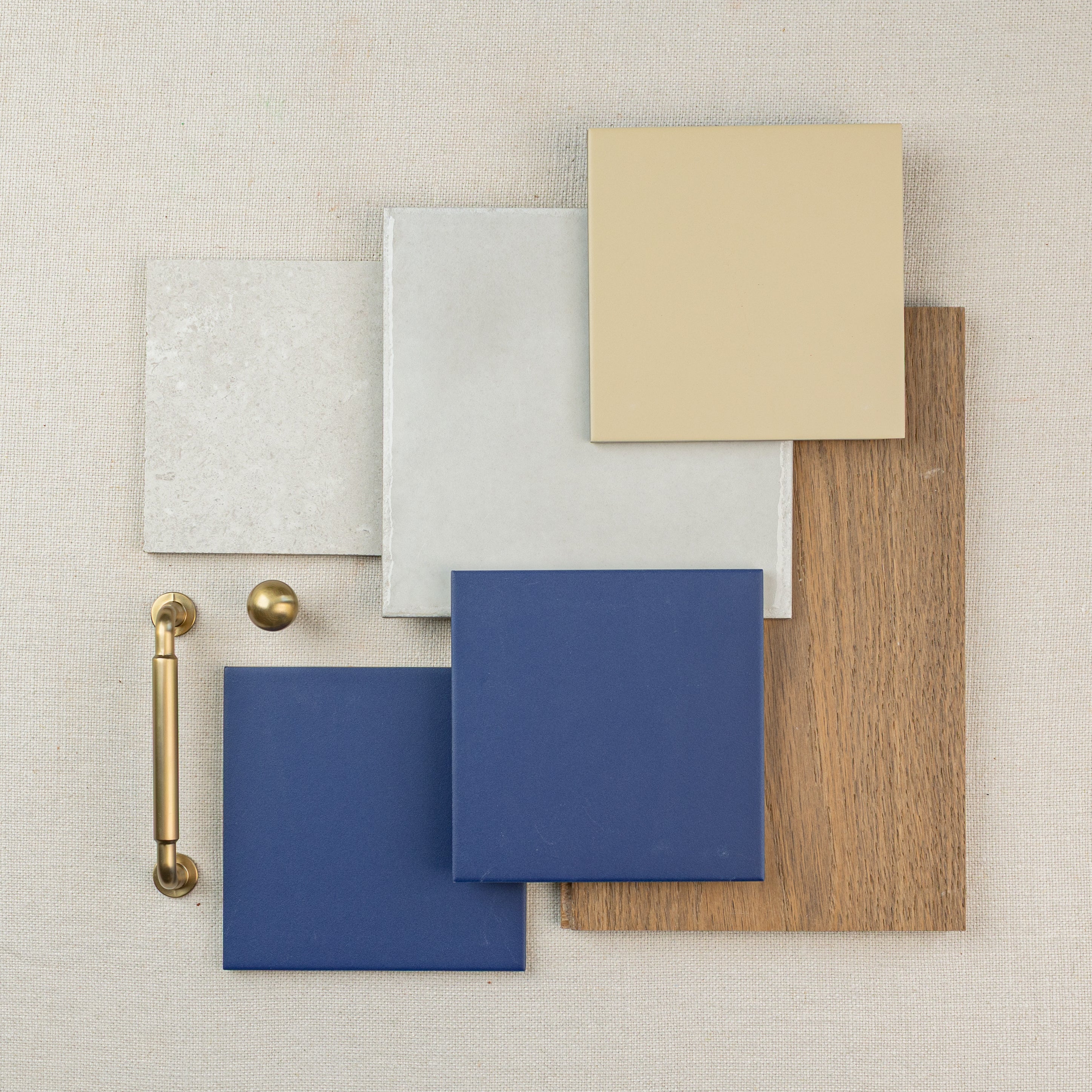 Assortment of ceramic tile samples in neutral and blue tones with a wood piece and brass hardware on fabric background