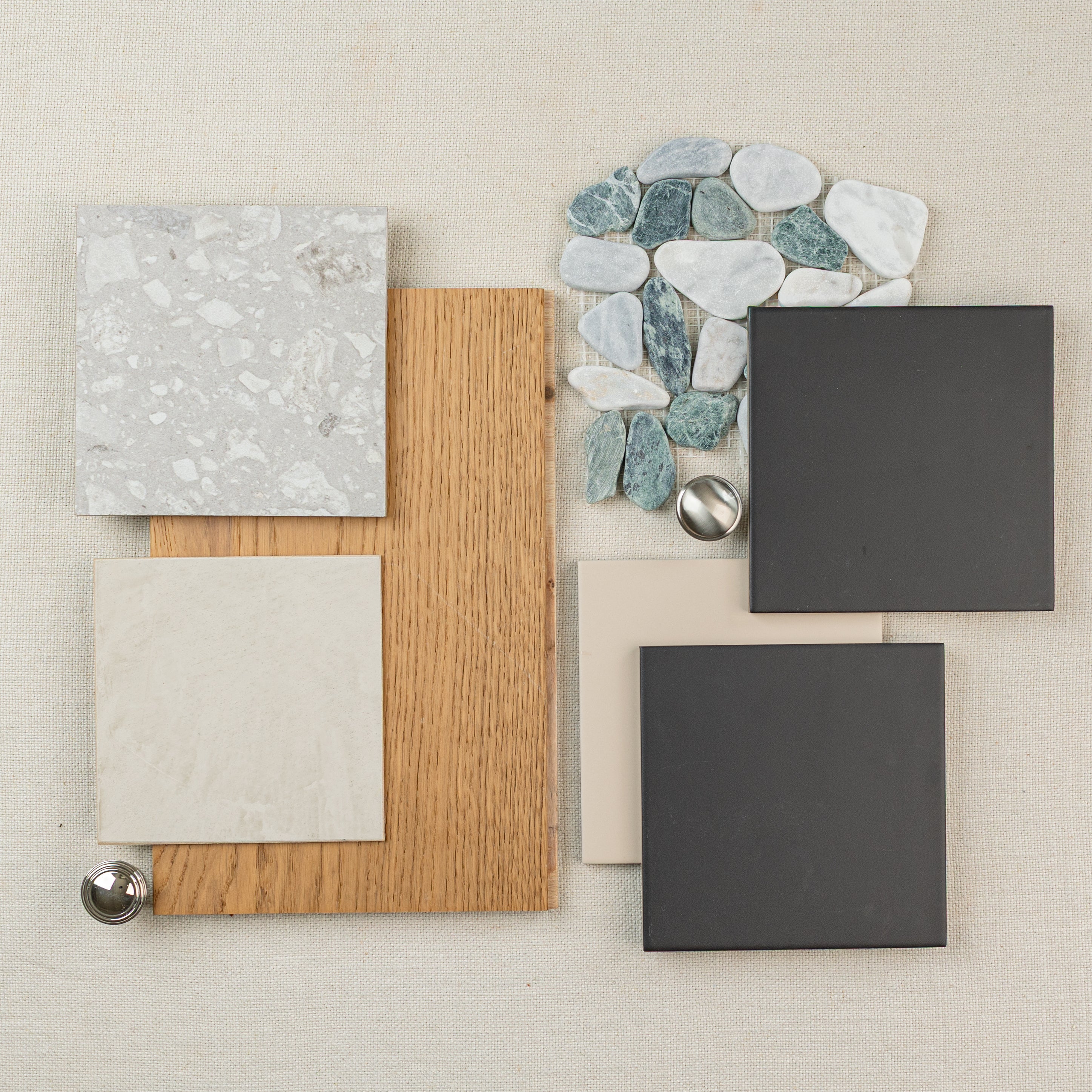 Flat lay of tile samples, engineered wood flooring, and natural stone pebbles on linen fabric background