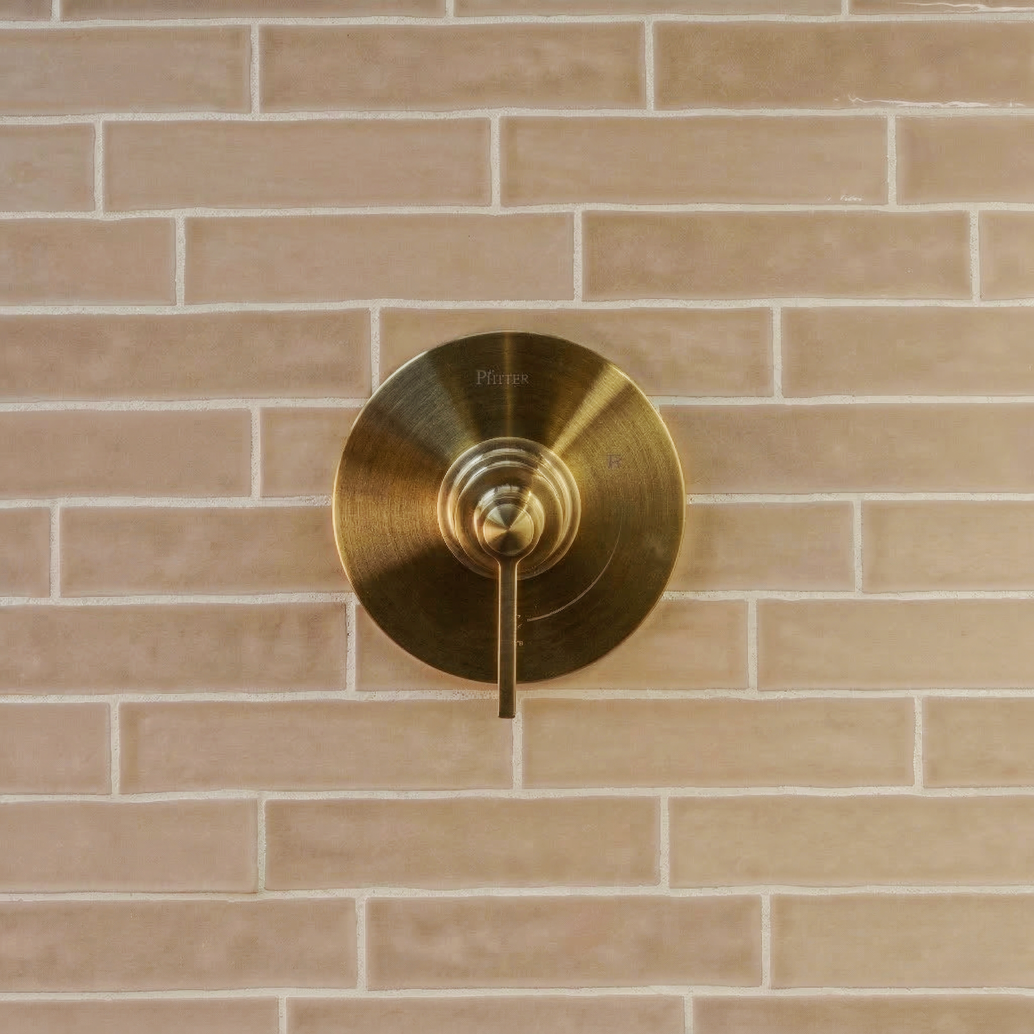 Matte light brown ceramic tiles in a horizontal subway layout with a centered round brass faucet handle