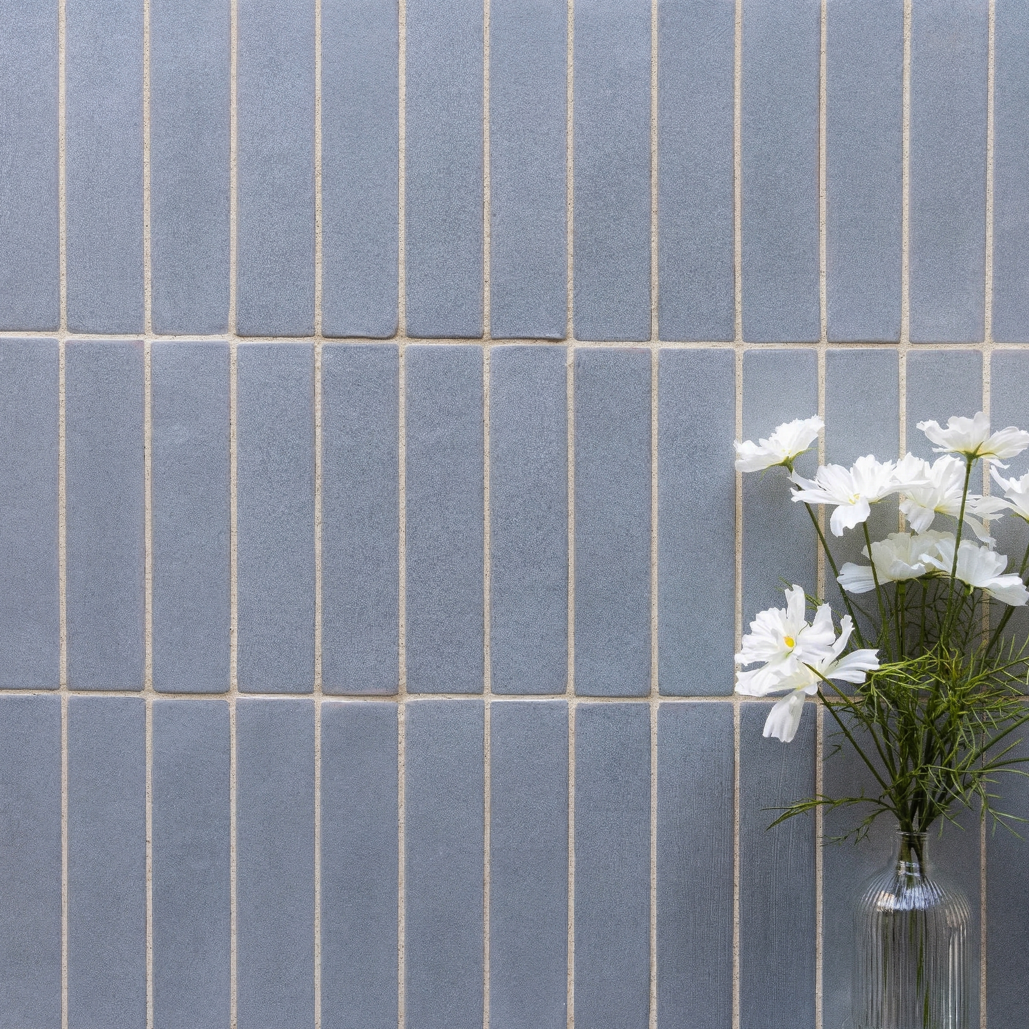 Matte blue rectangular ceramic tiles with visible grout lines and white daisies in a clear glass vase nearby