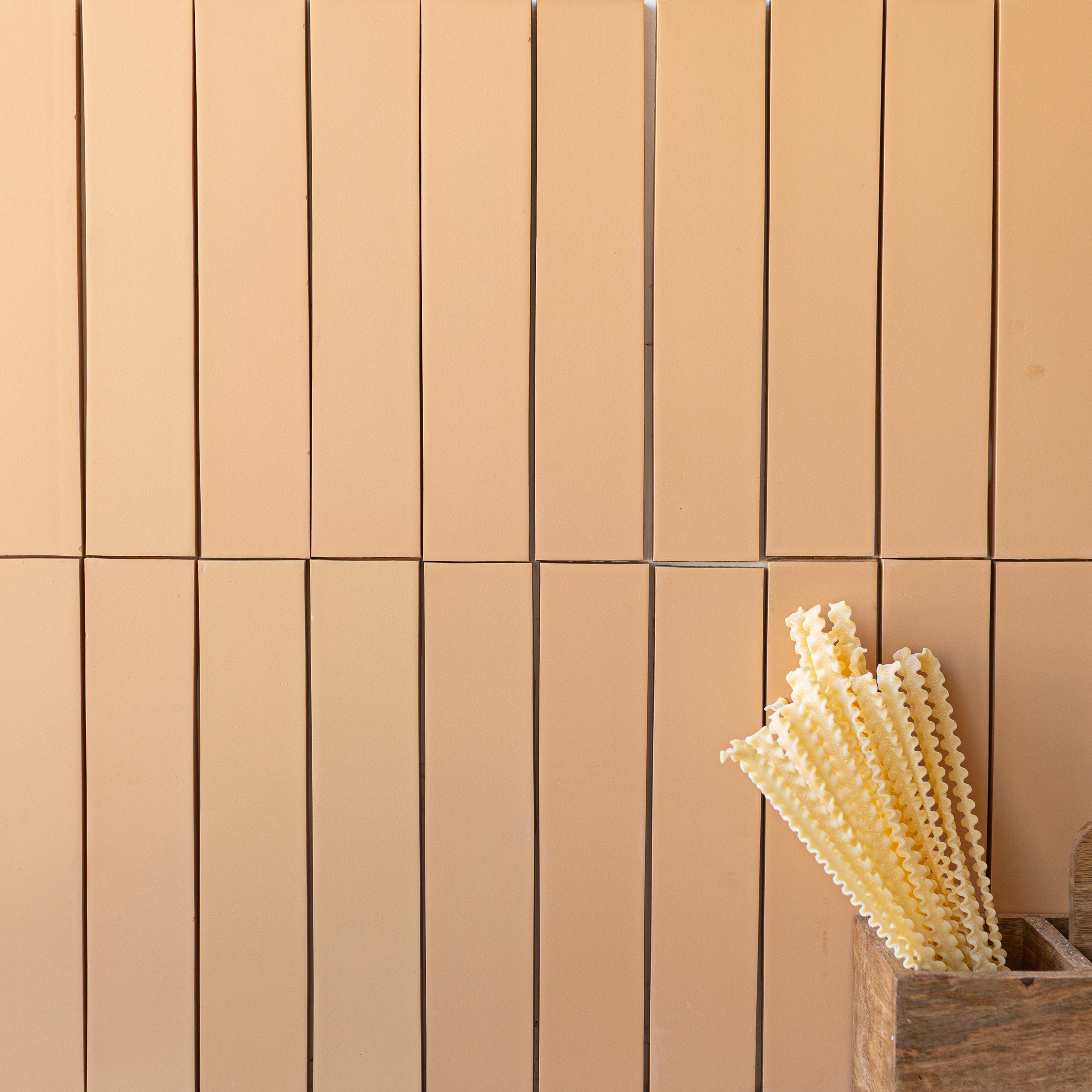 Beige rectangular ceramic tiles with a smooth matte finish alongside a wooden container holding textured pasta strands