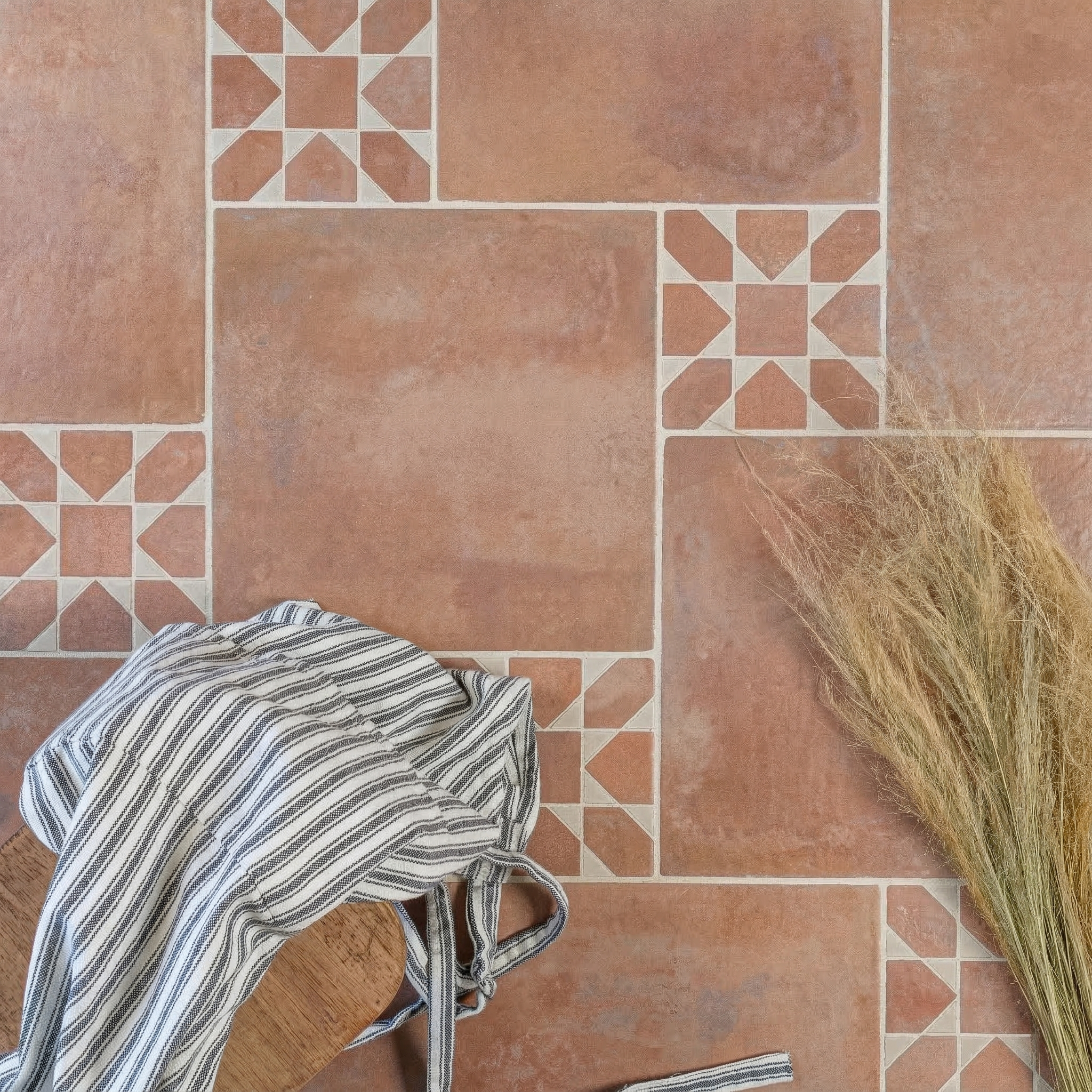 Large terracotta-style ceramic tiles with geometric patterned insets, accompanied by a striped cloth and dried grasses.