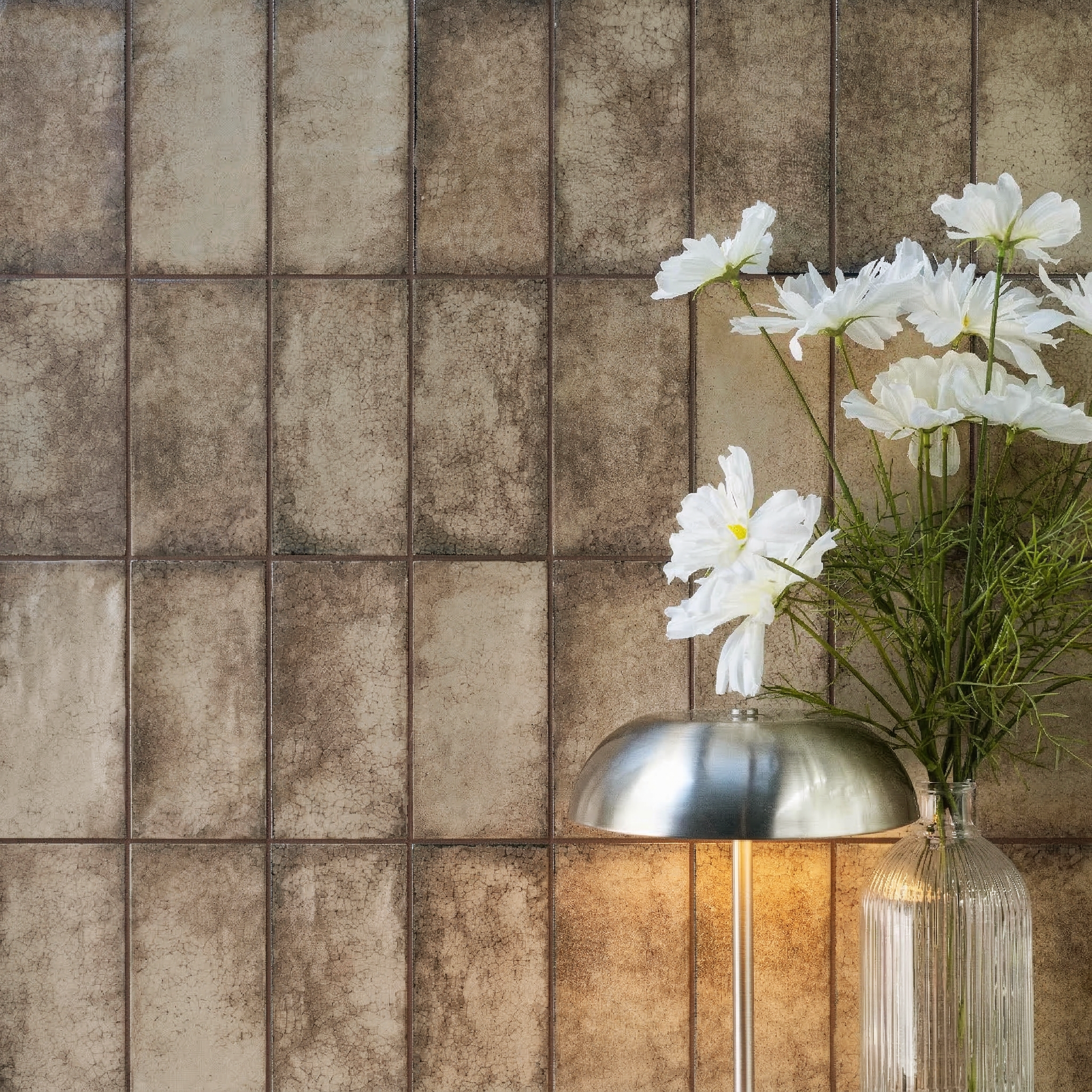 Vertical rectangular textured ceramic tiles in muted sand and brown with a modern silver lamp and white flowers nearby