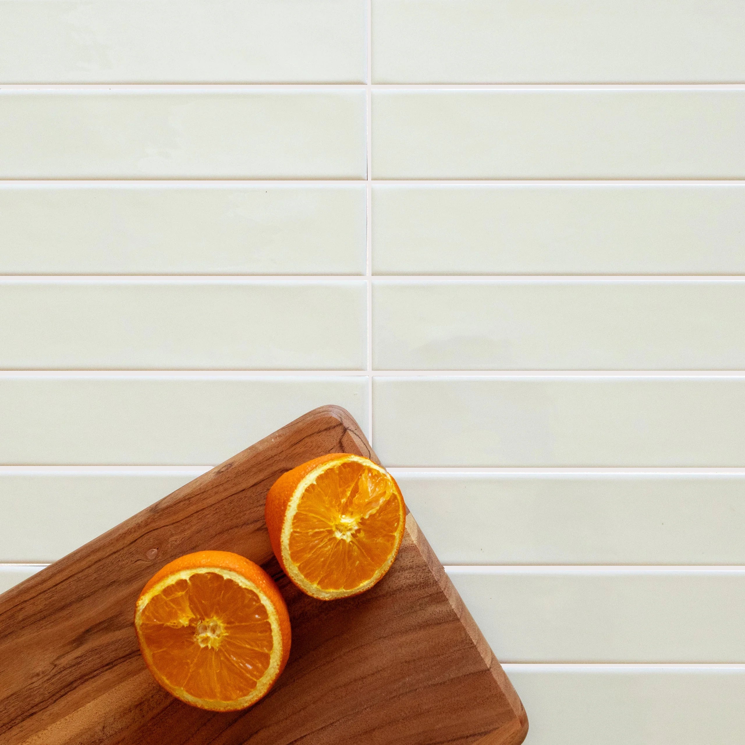 Glossy cream ceramic tiles arranged horizontally with a wooden board holding two halves of a fresh orange