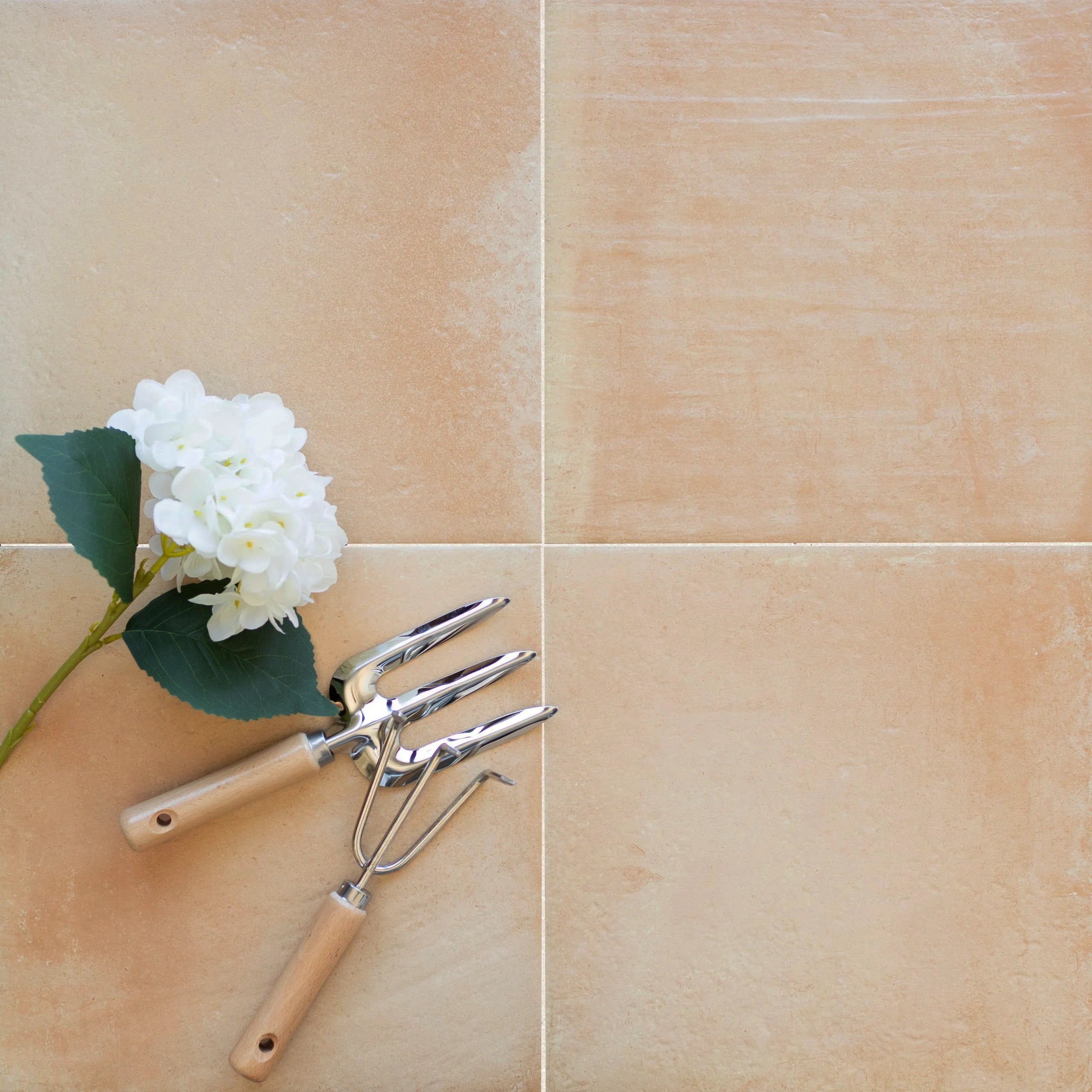 Soft cream matte porcelain tiles arranged in a square grid with gardening tools and a white hydrangea bloom nearby