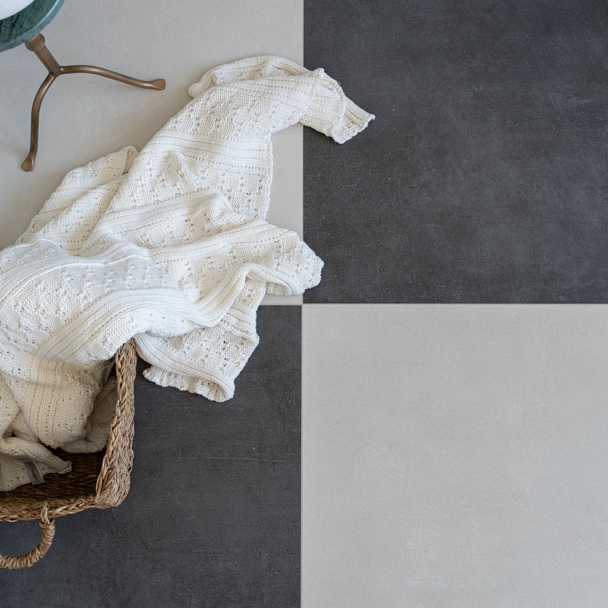 Flat lay of dark gray and light gray square tiles beside a white knitted blanket in a woven basket