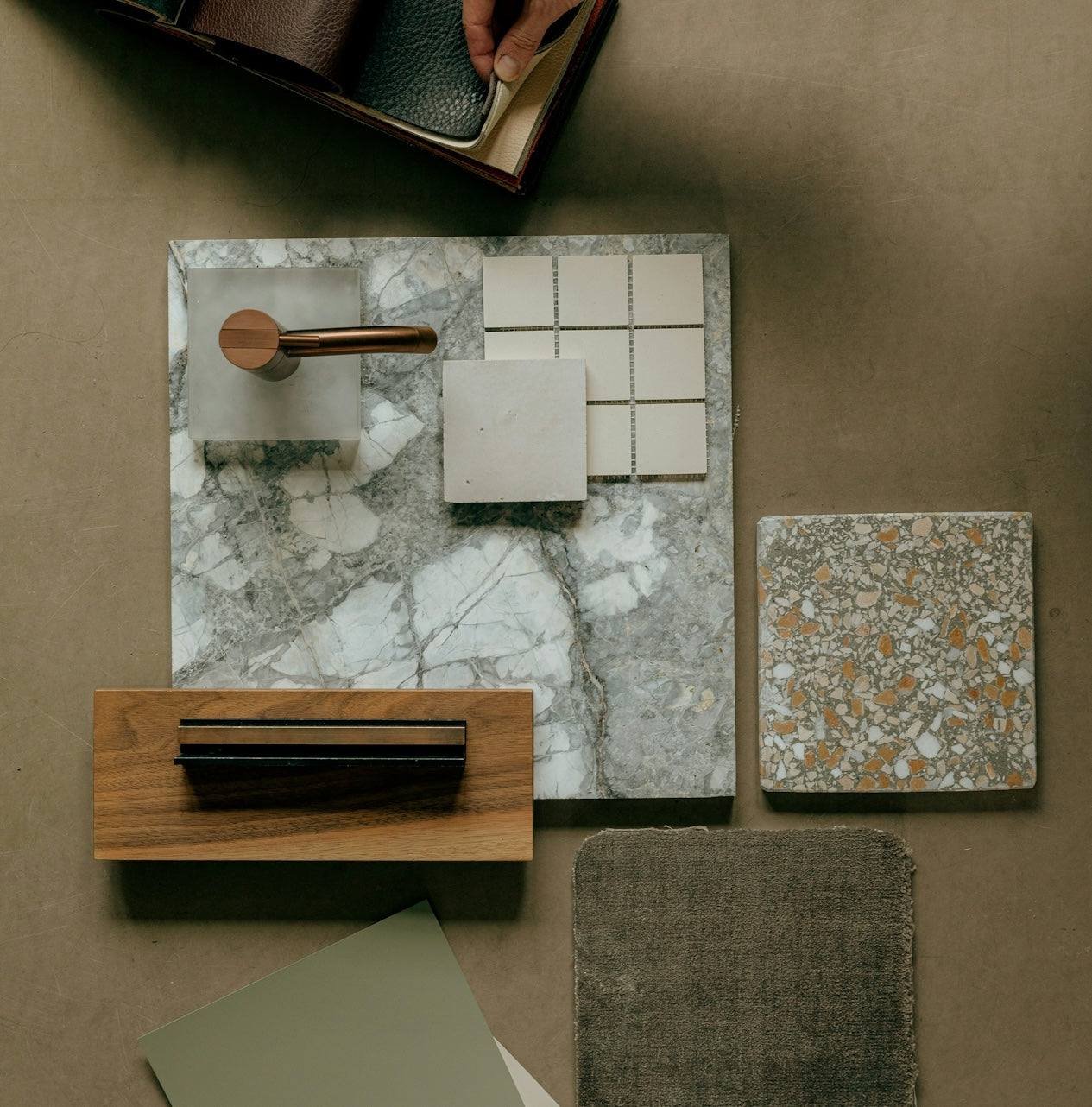 Overhead view of marble slabs, wood and fabric samples, and white square tiles arranged on a neutral surface