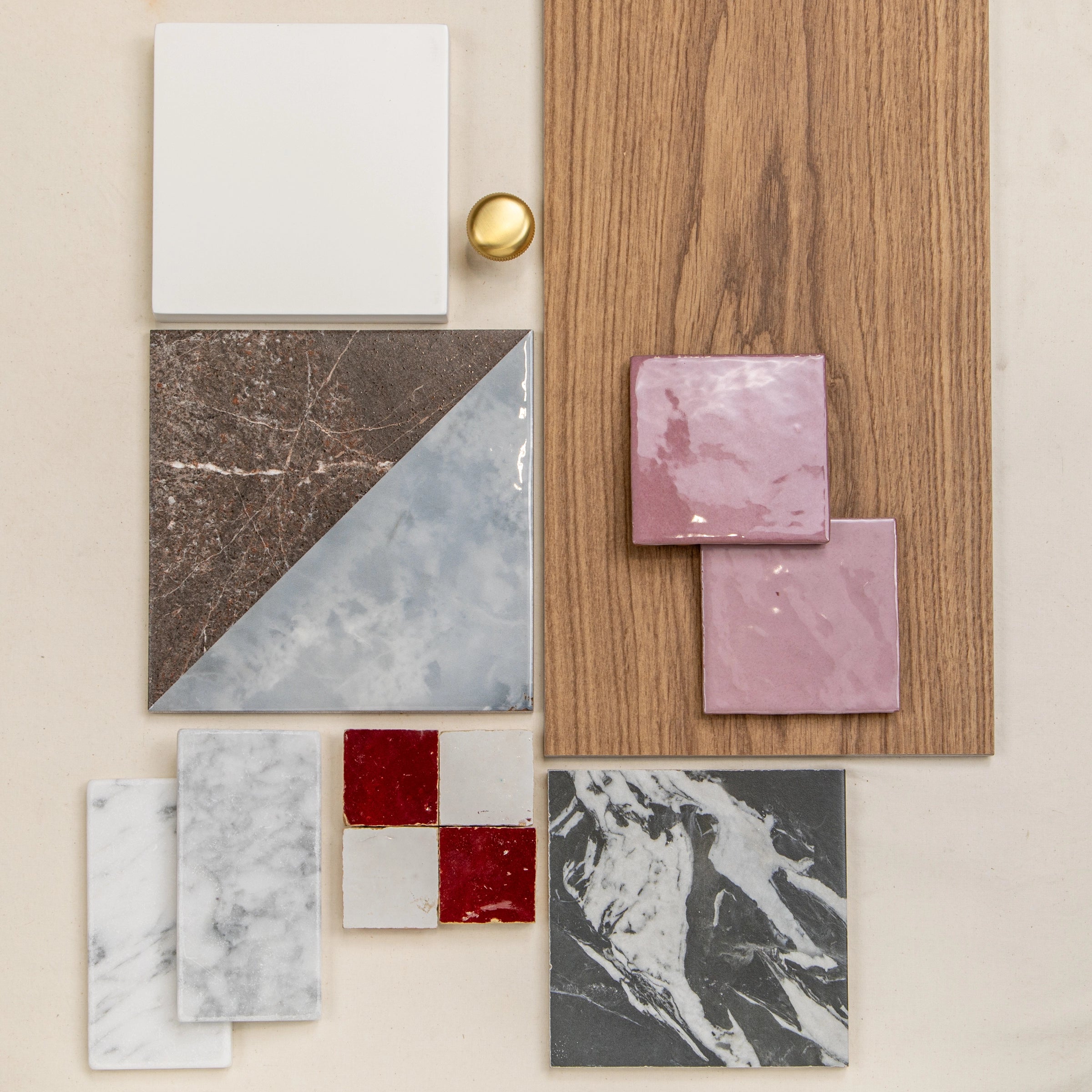 Flat lay of ceramic tiles with marble and solid colors, wood plank, pink square tiles, and brass hardware on neutral background