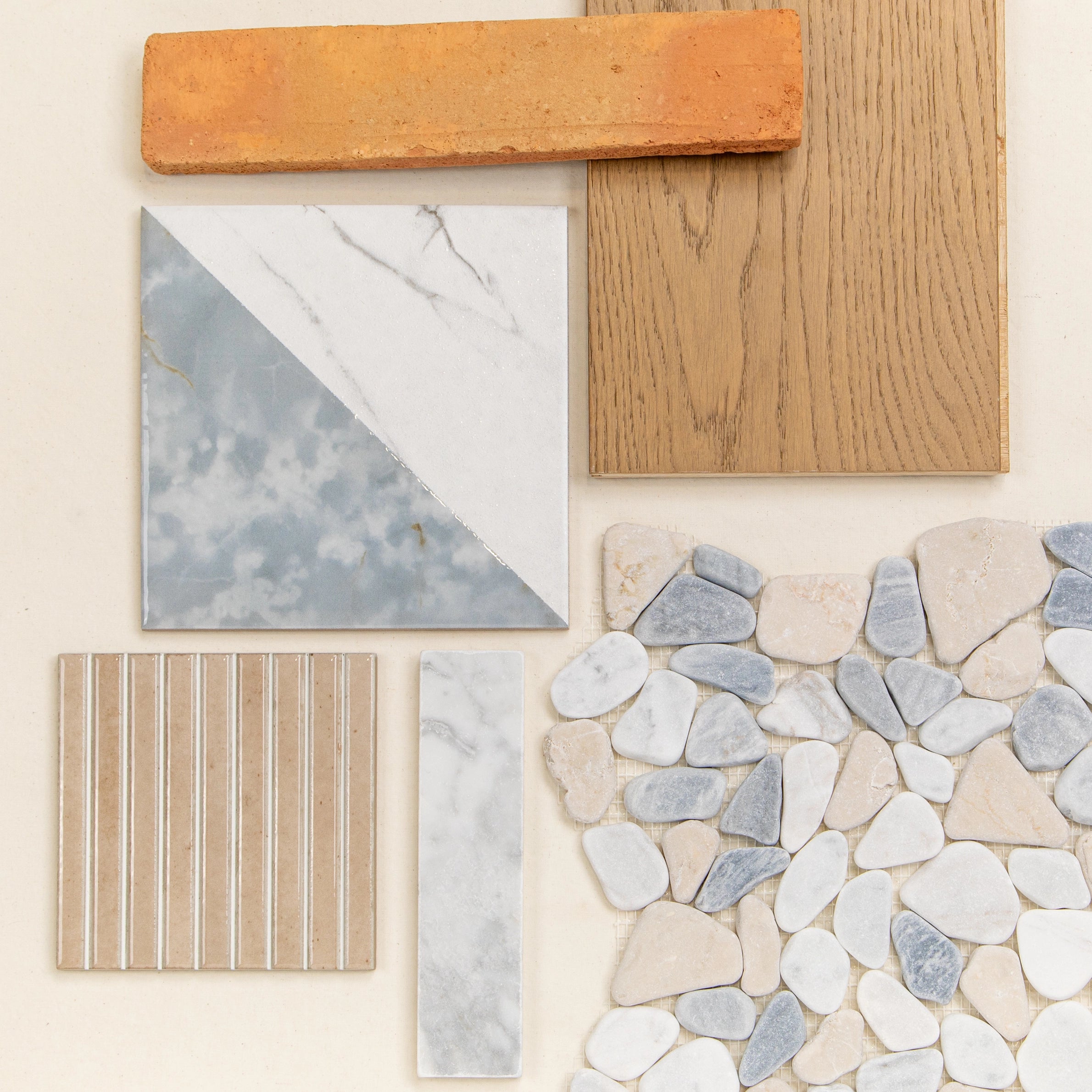 Flat lay of terracotta brick, wood sample, marble-look porcelain tile, pebble mosaic, and beige striped ceramic tile pieces