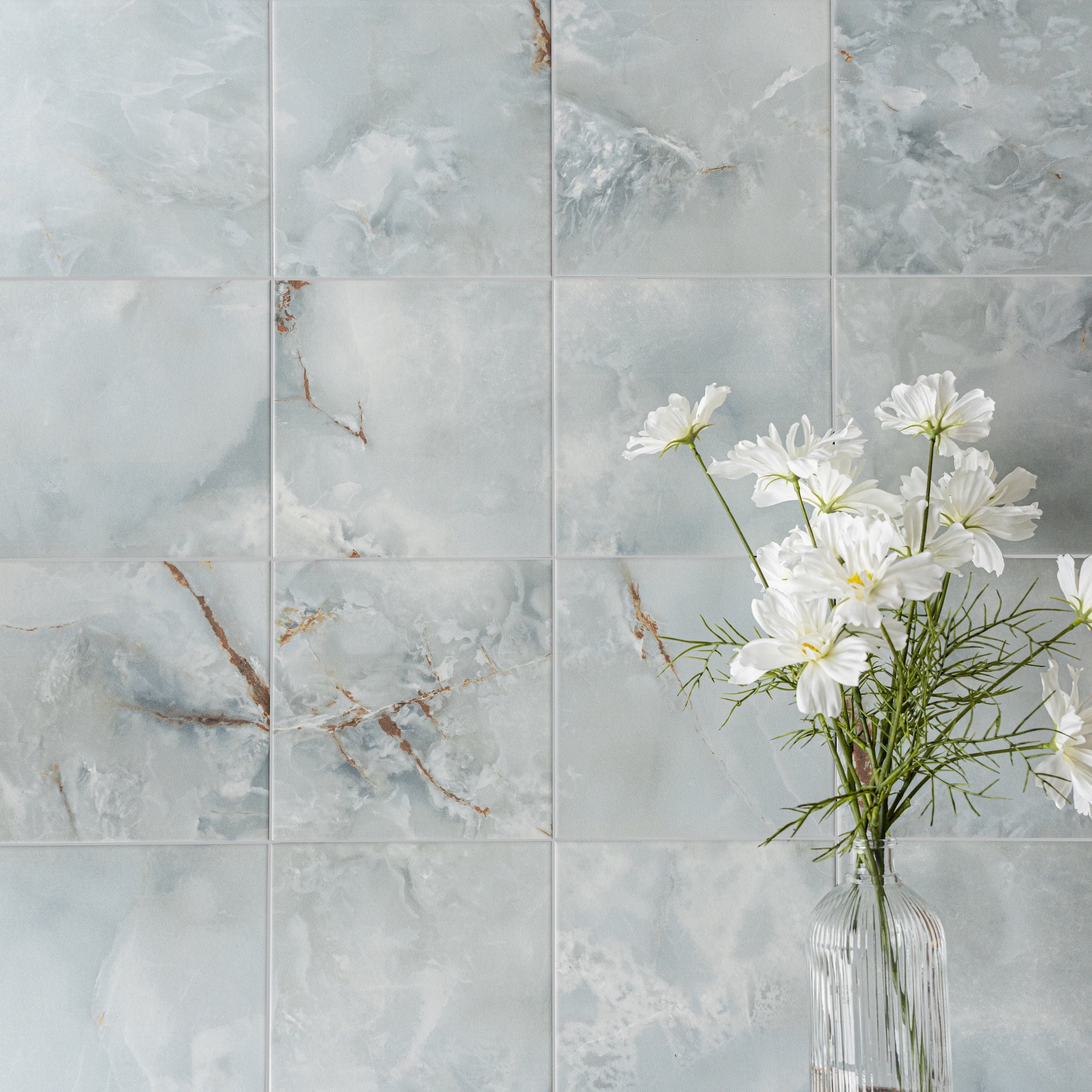 Soft gray porcelain tiles with subtle brown veining arranged in a grid behind a clear vase with white flowers