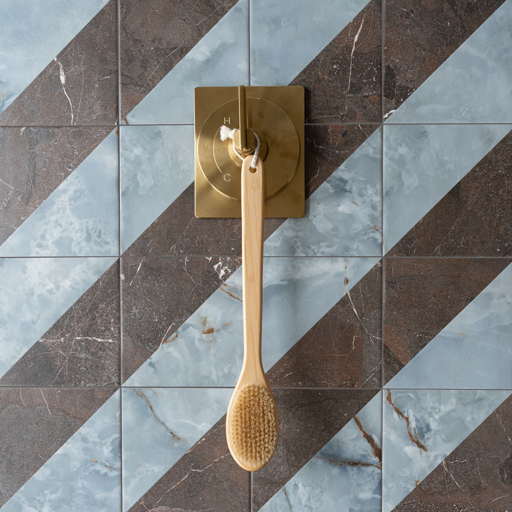 Diagonal pattern of blue and brown marble-effect porcelain tiles with a brass shower control and wooden brush hanging