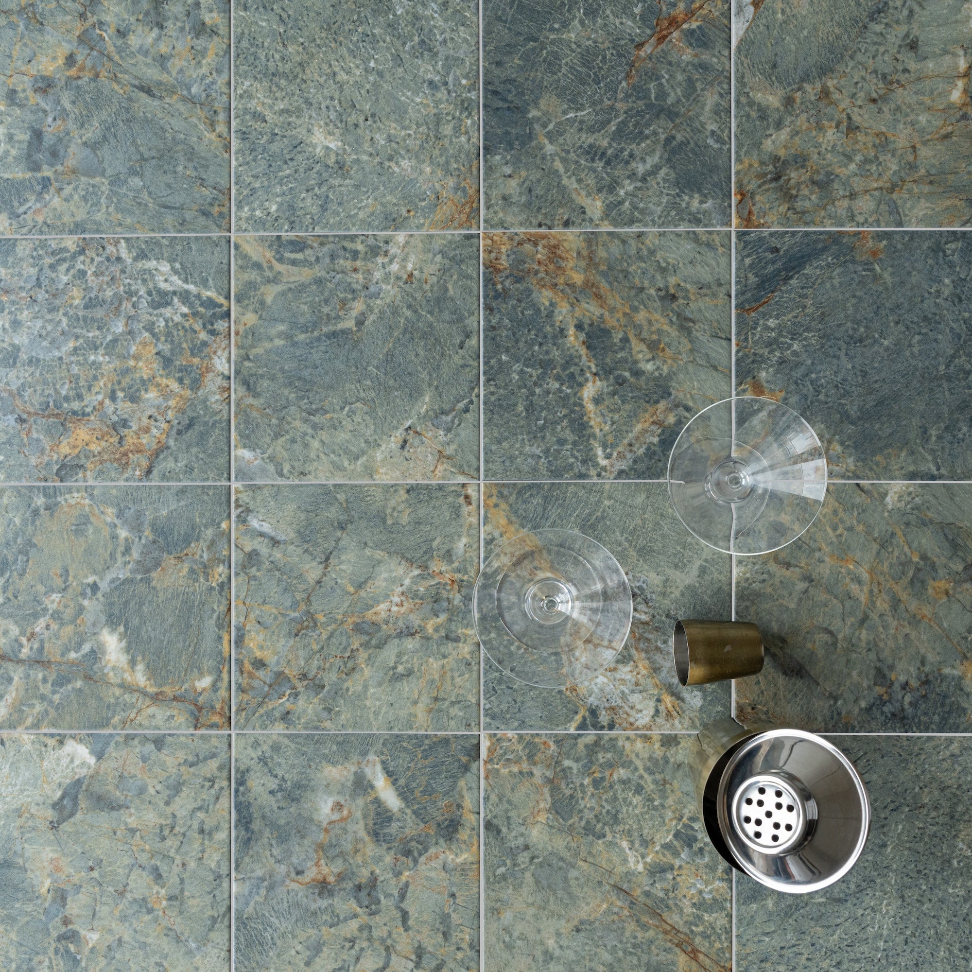 Close-up of textured natural stone tiles with green, gray, and brown tones and a metal shower squeegee attached by suction cups