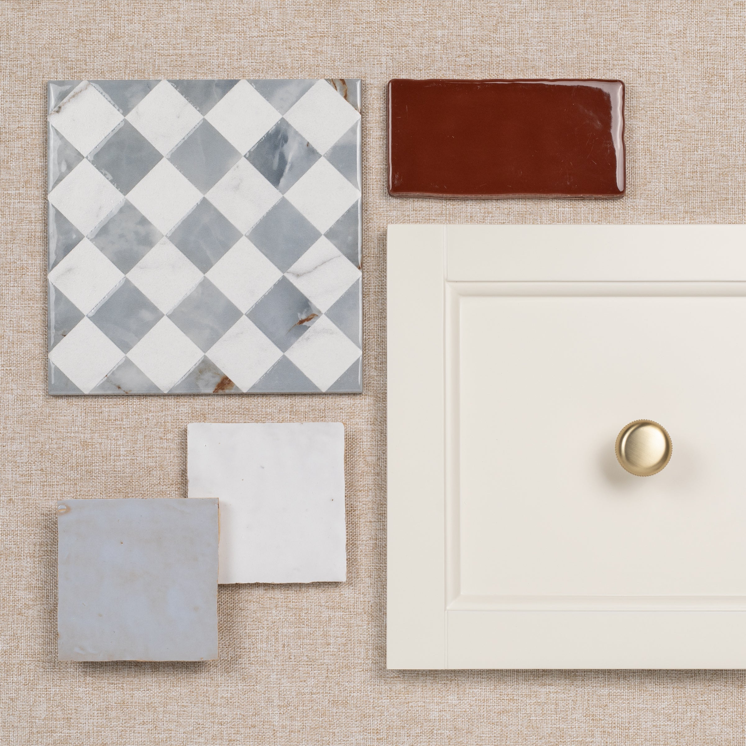 Flat lay of ceramic and porcelain tiles with a white cabinet door and brass knob on a textured surface