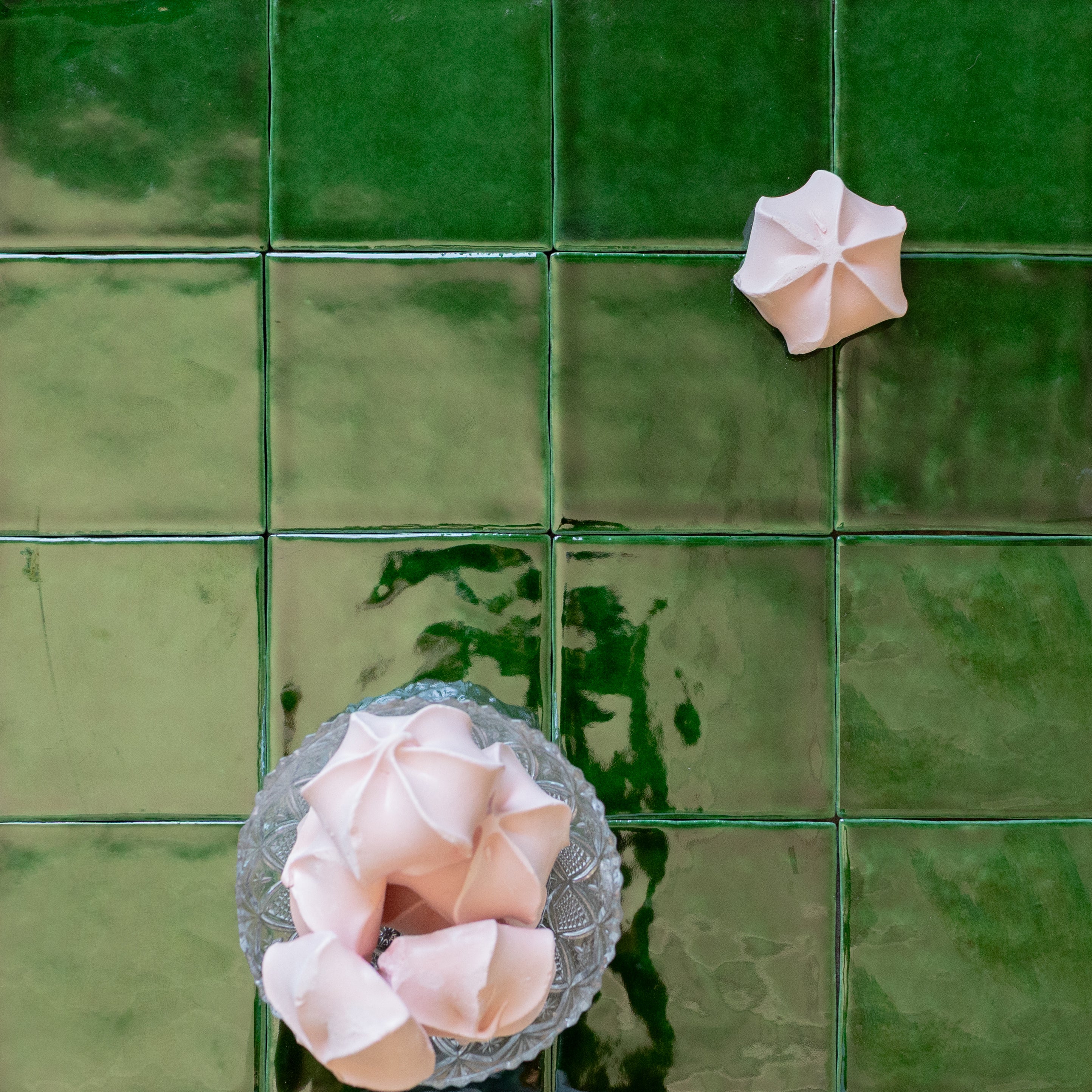 Glossy deep emerald ceramic tiles with a clear bowl holding soft pale pink decorative petals on top