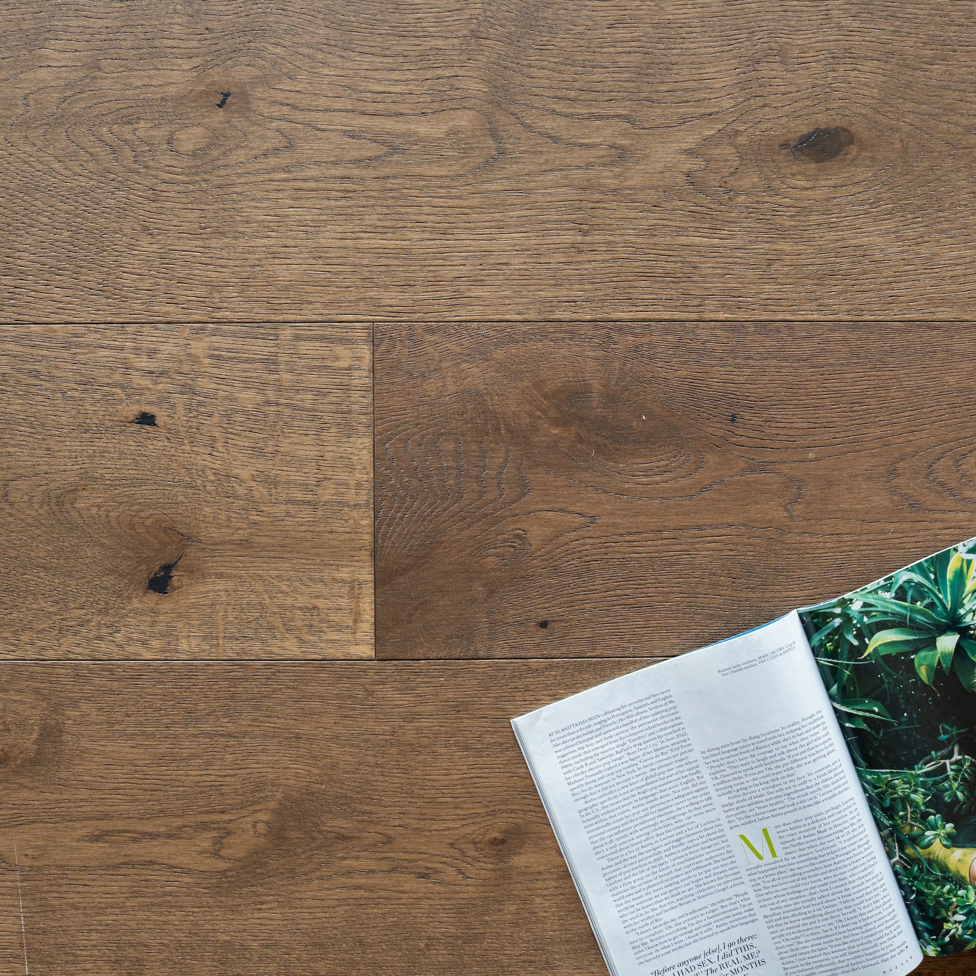 Warm-toned engineered oak wood planks with distinct grain and knots beside an open magazine featuring greenery images