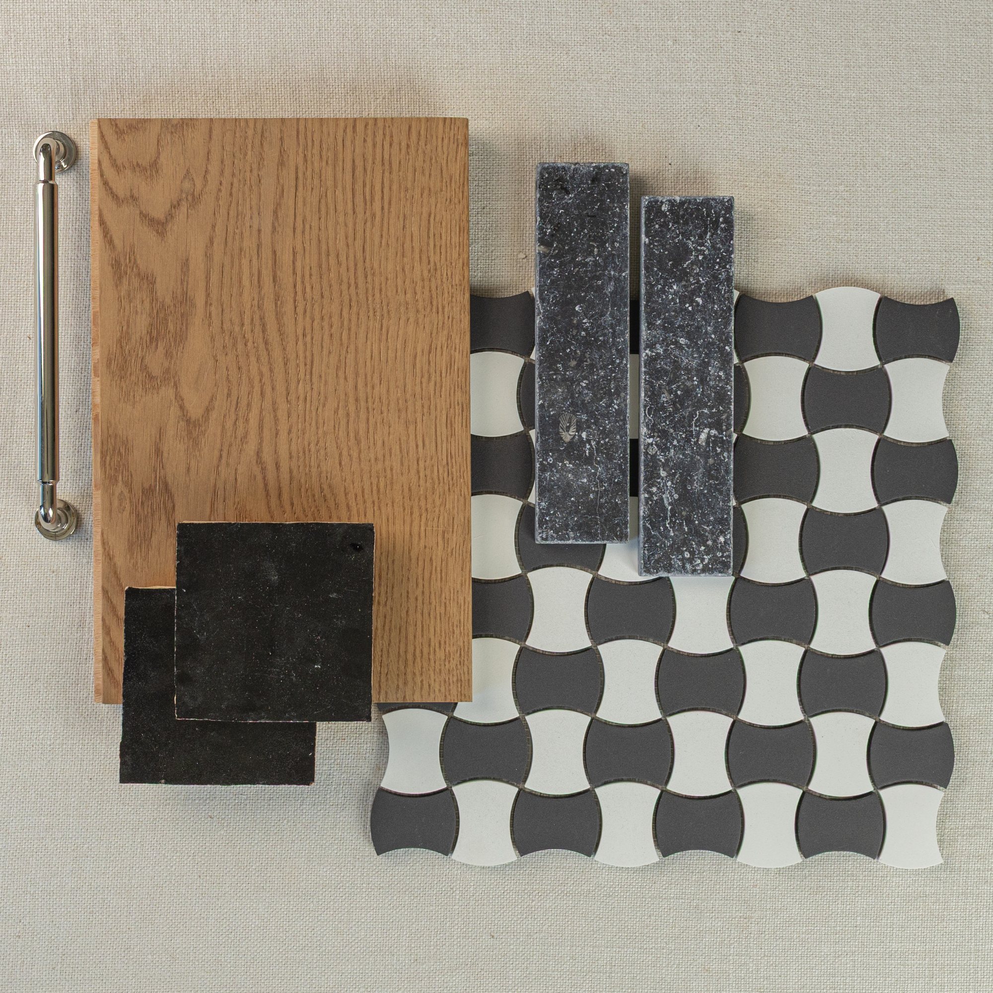 Flat lay of oak wood sample, black square tiles, dark textured rectangular tiles, and black and white patterned mosaic on beige fabric