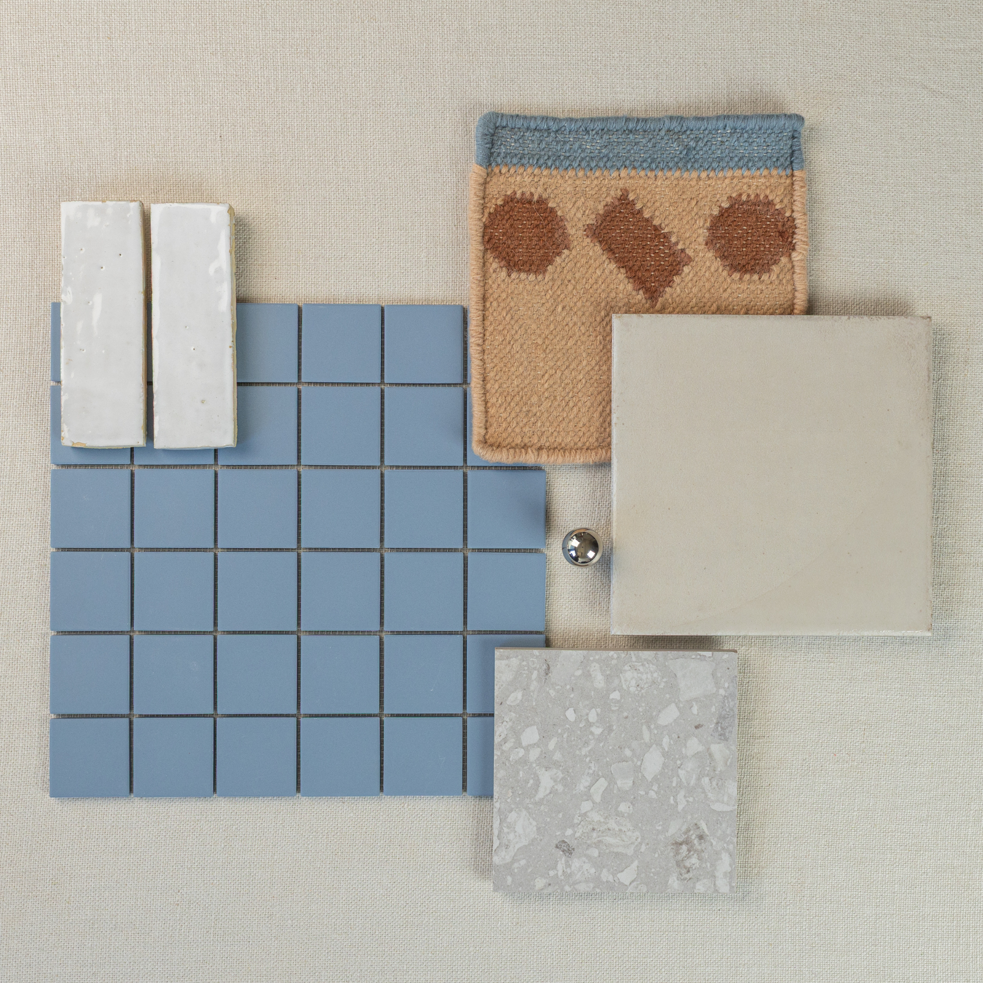 Overhead view of blue ceramic mosaic tile, beige large tile, terrazzo sample, patterned fabric, and white glazed bricks on neutral surface