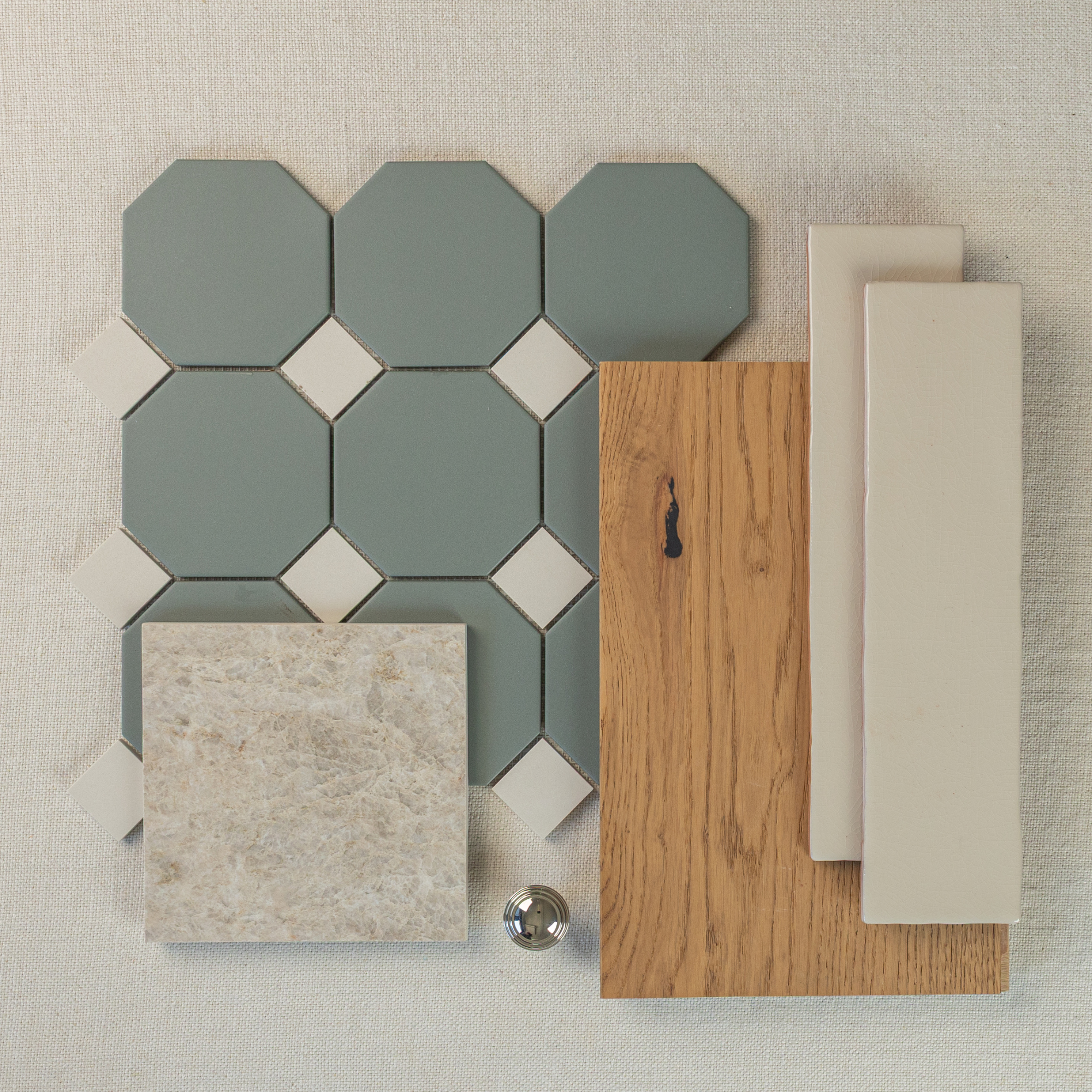 Flat lay of green octagon ceramic tiles with cream square accents, oak wood sample, beige rectangular tiles, and silver knob on fabric
