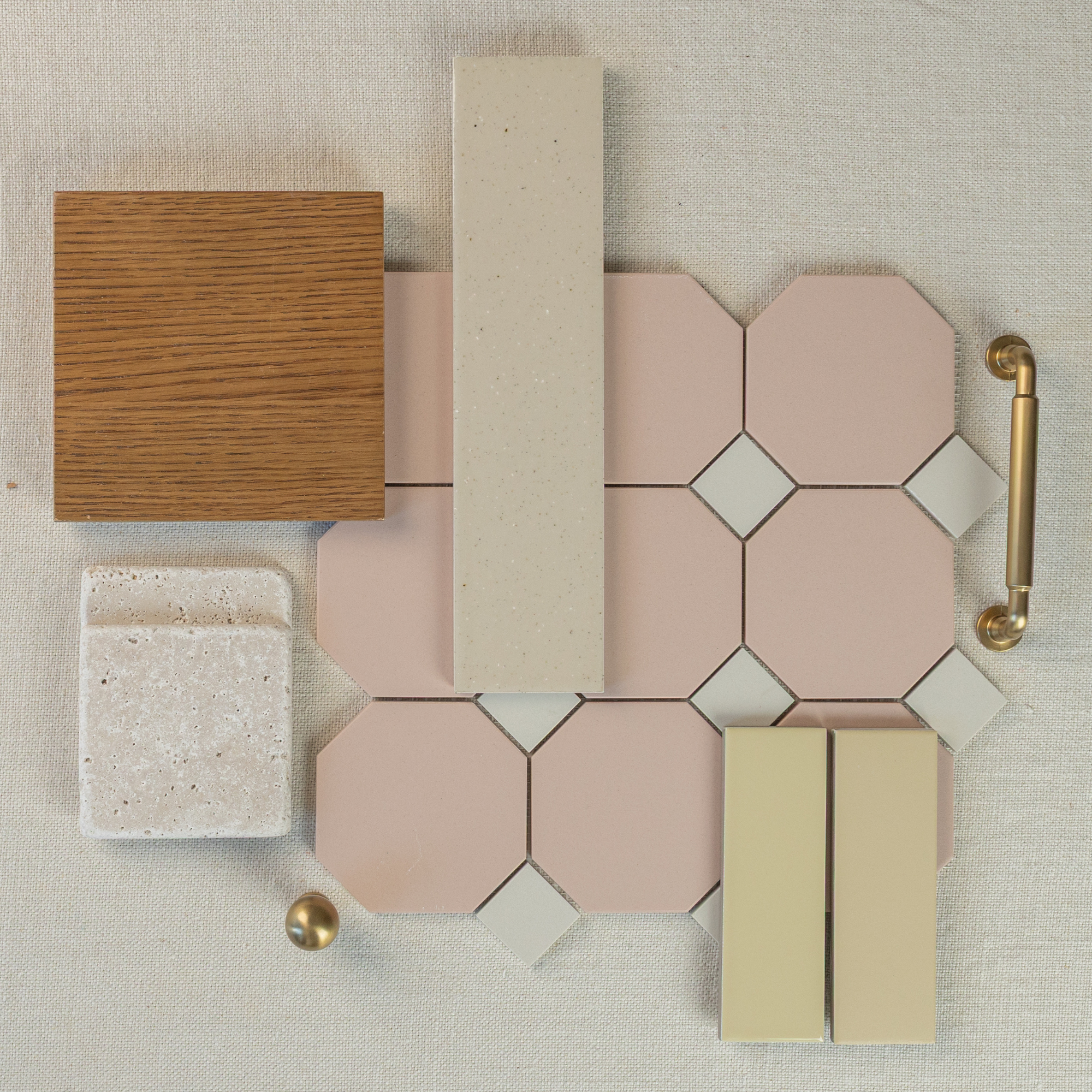 Flat lay of pink octagon porcelain tiles with cream and beige ceramic samples, oak wood, brass handle, and textured fabric background