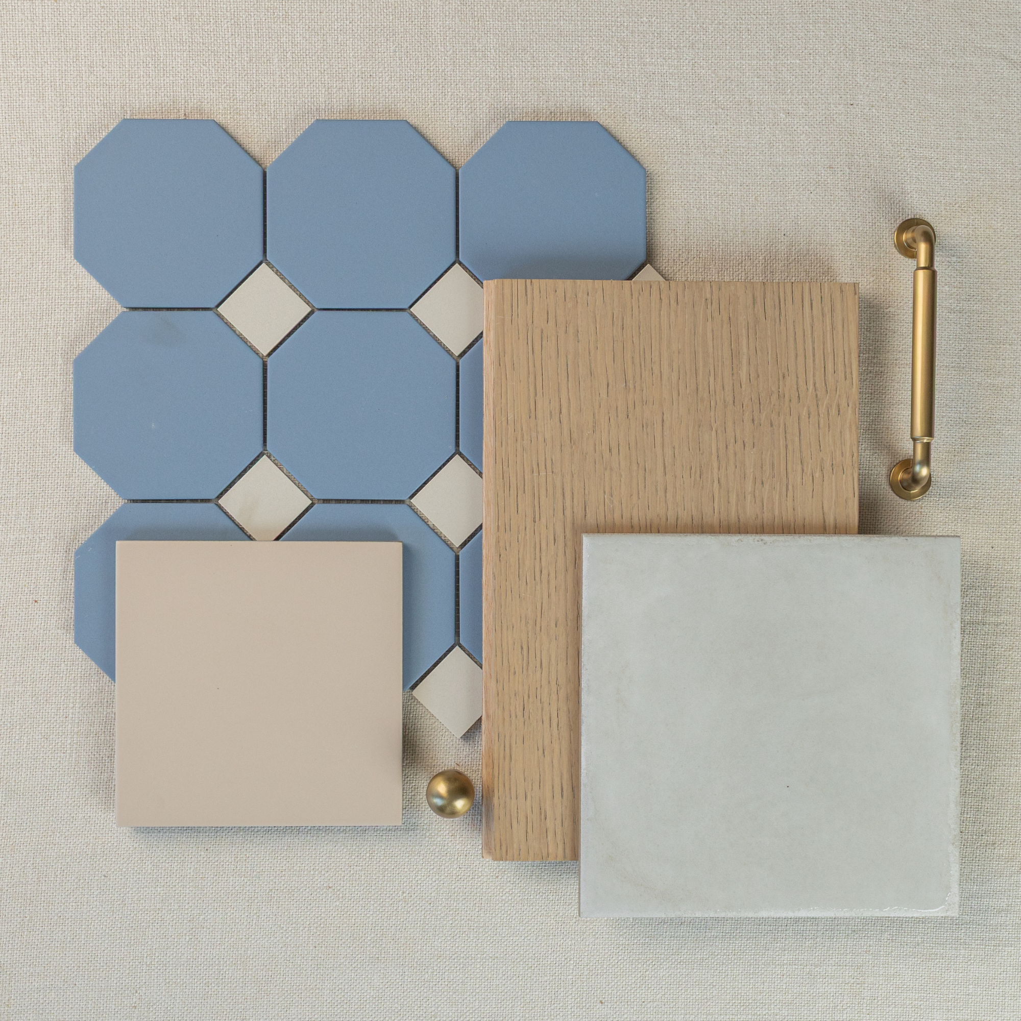 Arrangement of blue octagon and beige diamond ceramic tiles, oak wood sample, smooth beige and light gray tiles, and brass hardware on fabric