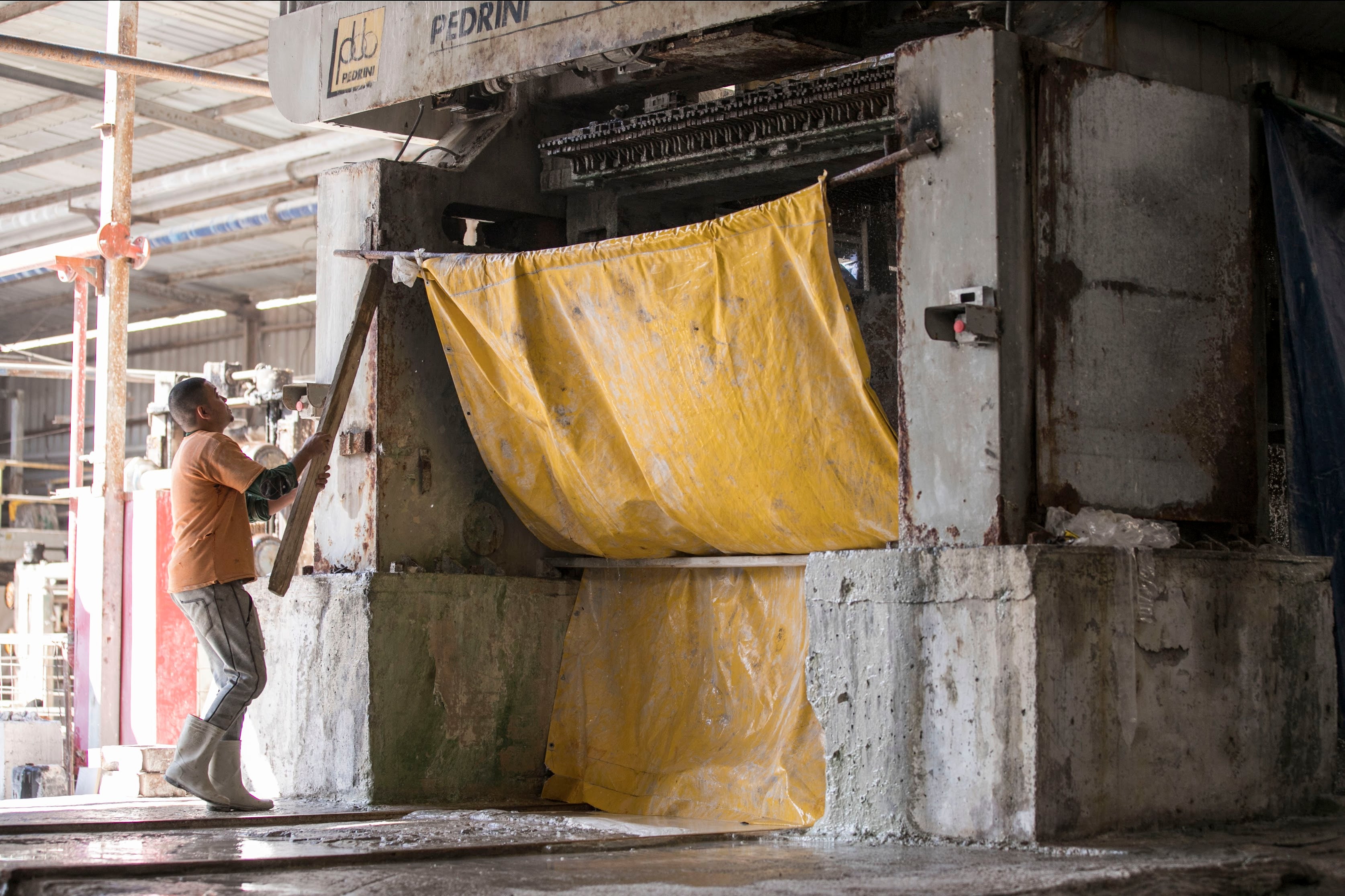 Worker operating large industrial machinery inside a factory with concrete and metal structures around