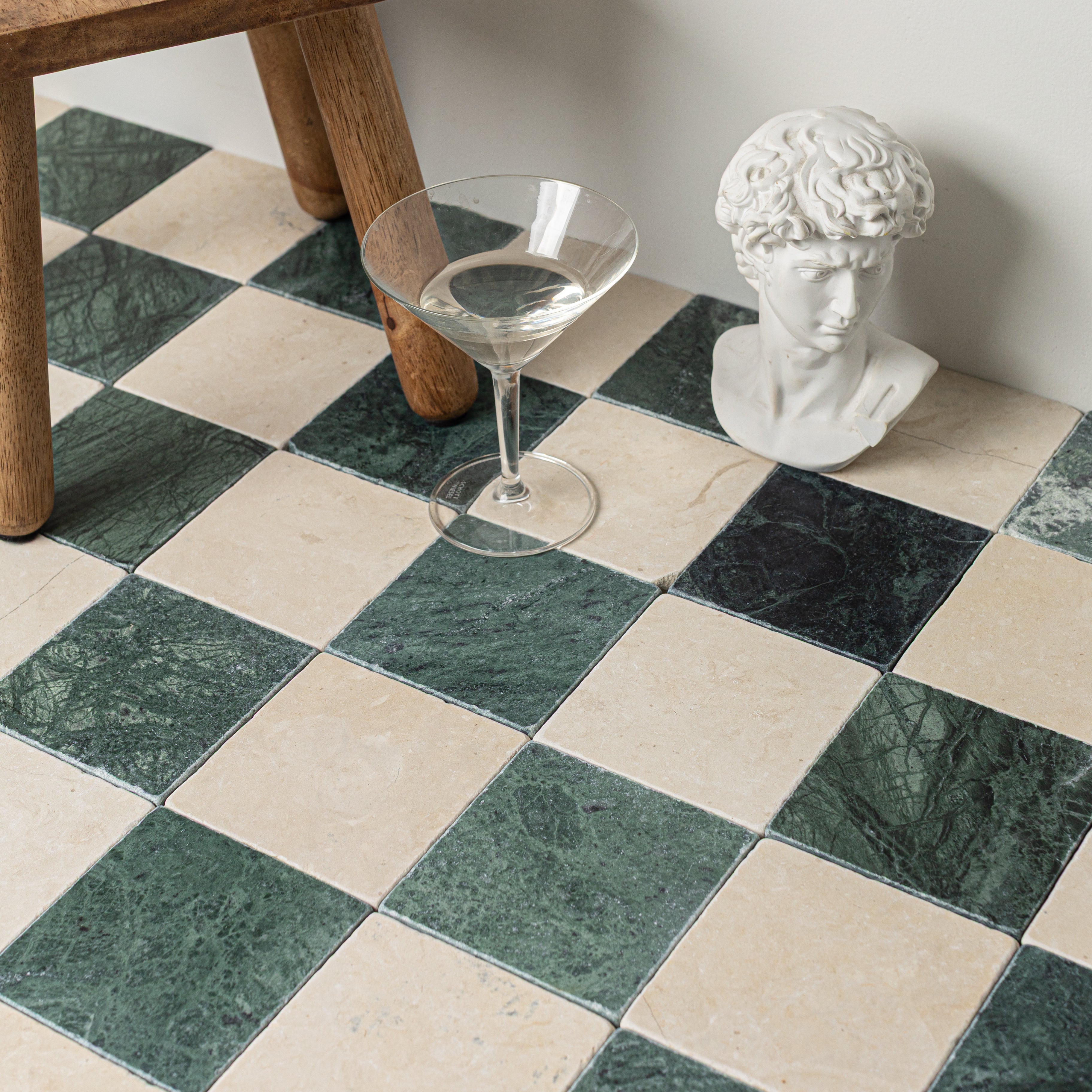 Checkerboard marble floor tiles in green and beige with a clear martini glass and classical white bust nearby