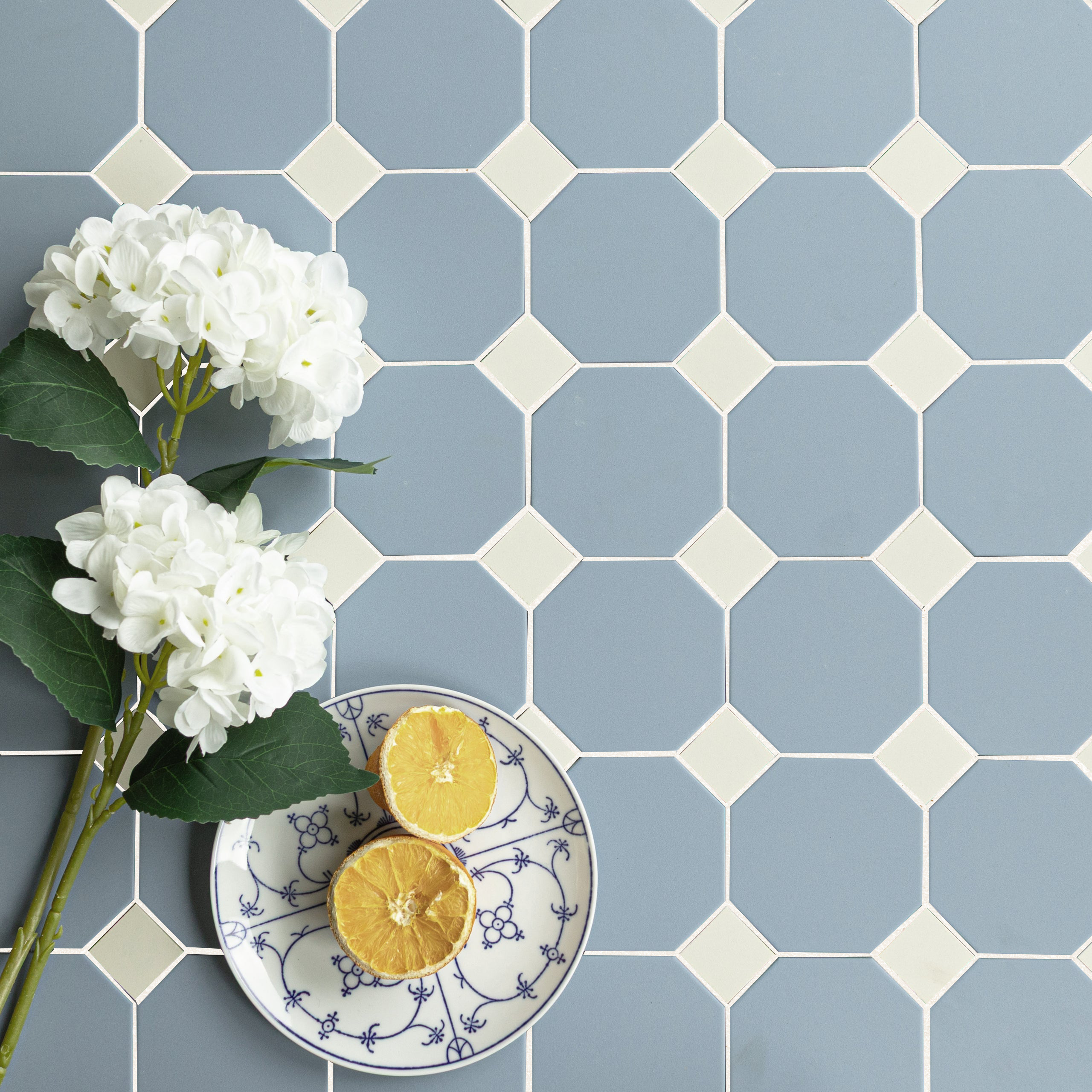 Octagon soft blue porcelain tiles with small cream diamond accents, styled with white flowers and a patterned plate holding two lemon halves