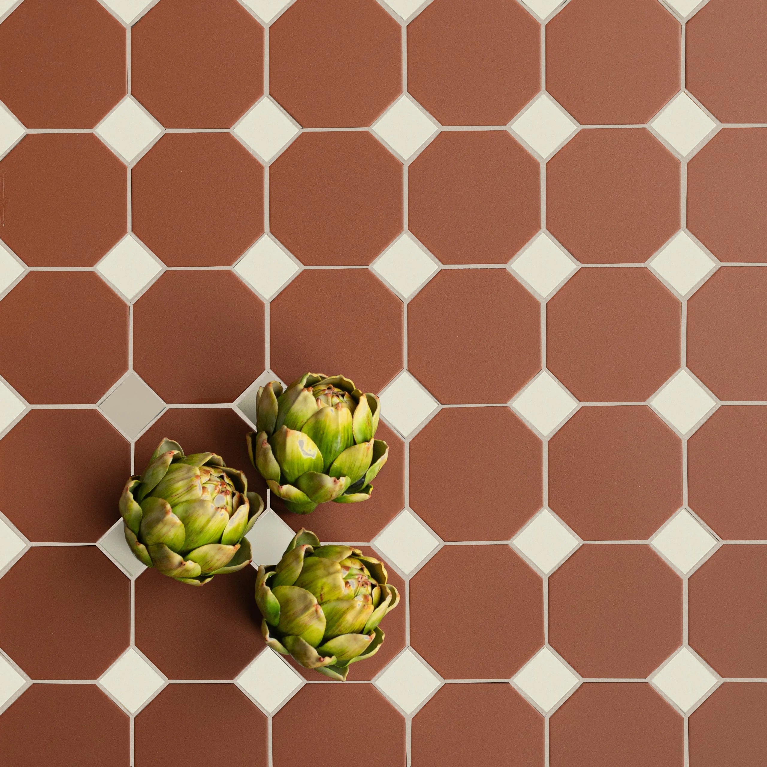 Flat lay of octagonal terracotta tiles with small cream diamond-shaped inserts and three artichokes placed on surface