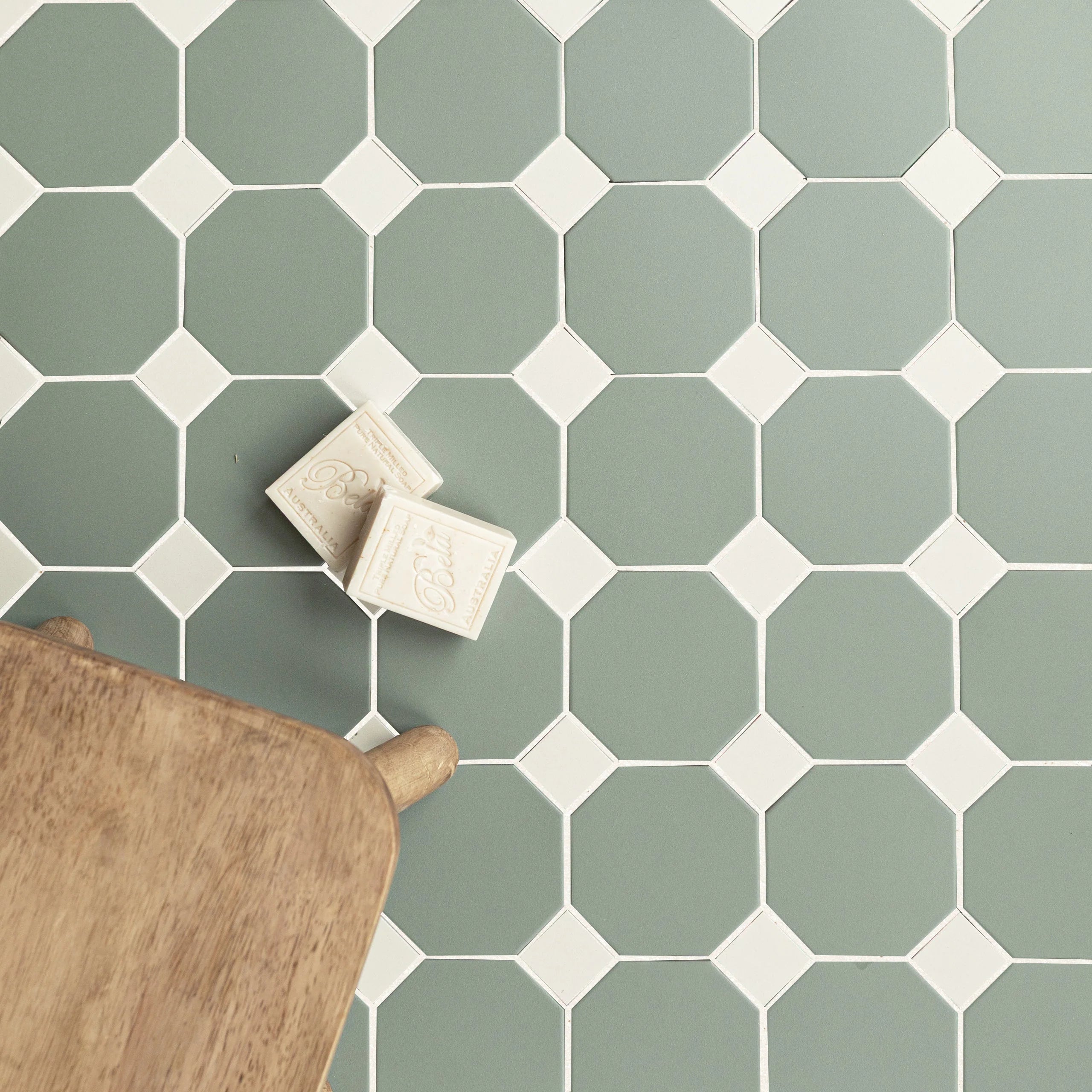 Matte sage green octagonal ceramic tiles paired with small cream square tiles and wooden chair leg visible