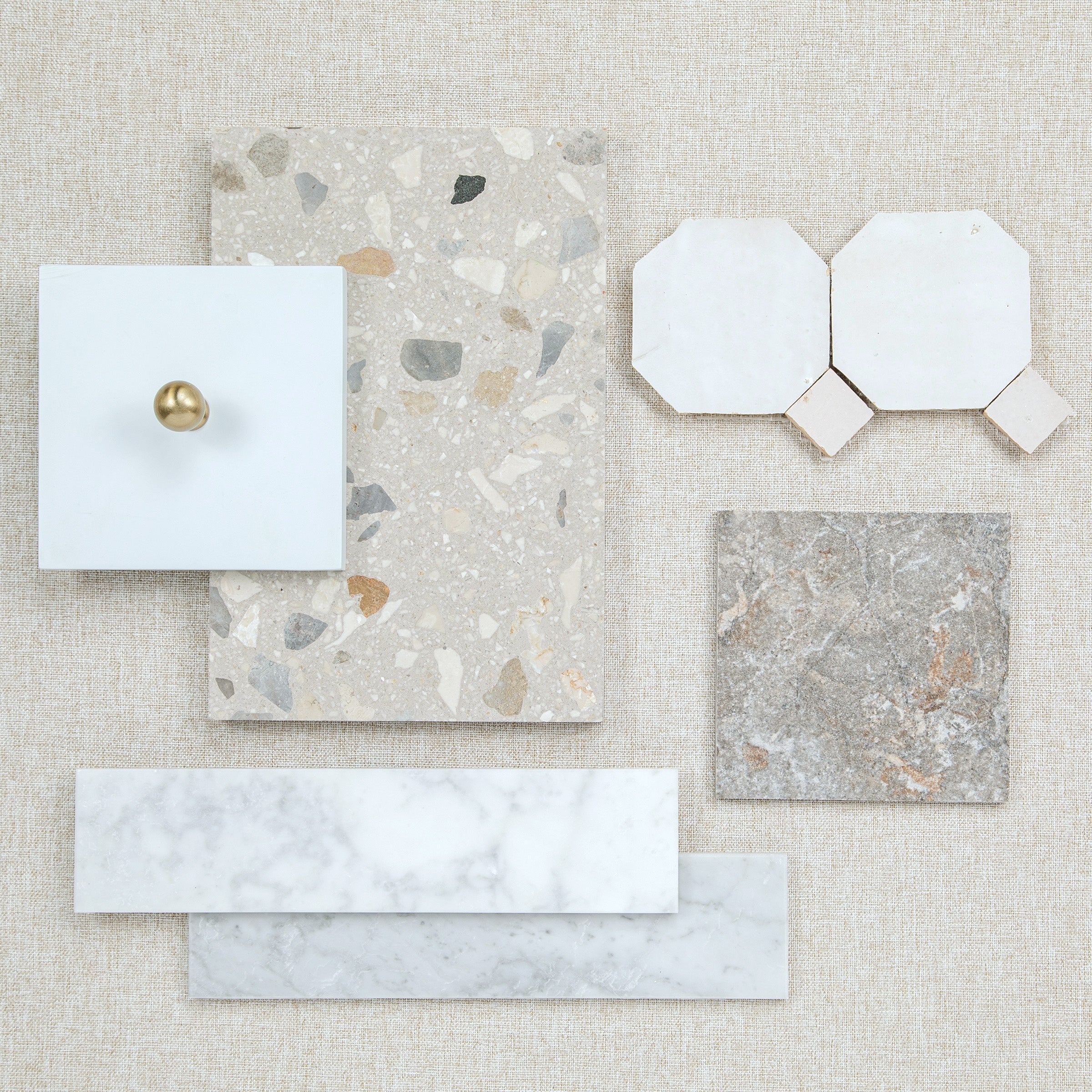 Neutral tile samples including terrazzo marble and geometric ceramic designs arranged on a fabric background