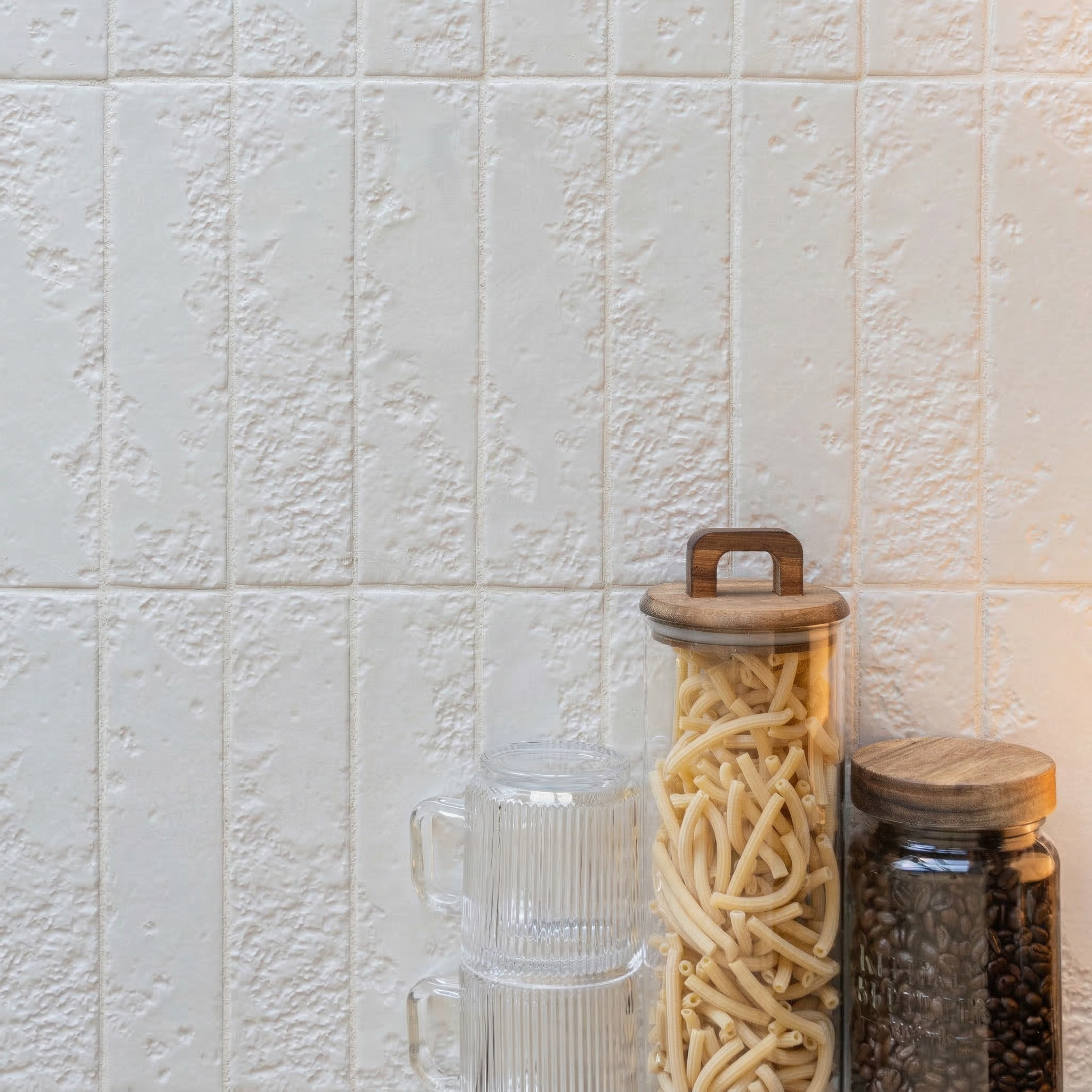 Textured vertical rectangular ceramic tiles in off-white shade with rustic finish beside glass jars of pasta and coffee beans