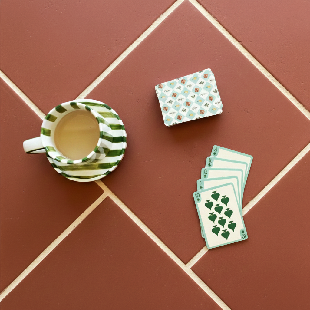 Square matte terracotta ceramic tiles with cream grout alongside a striped cup of tea and playing cards on top