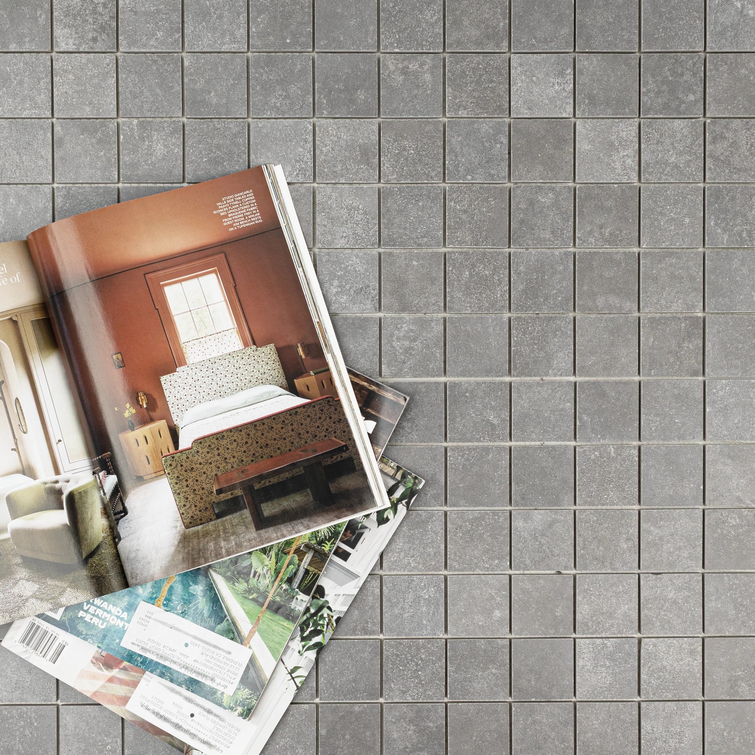 Square cement-look porcelain mosaic tiles in muted gray with a matte finish beneath open interior design magazines