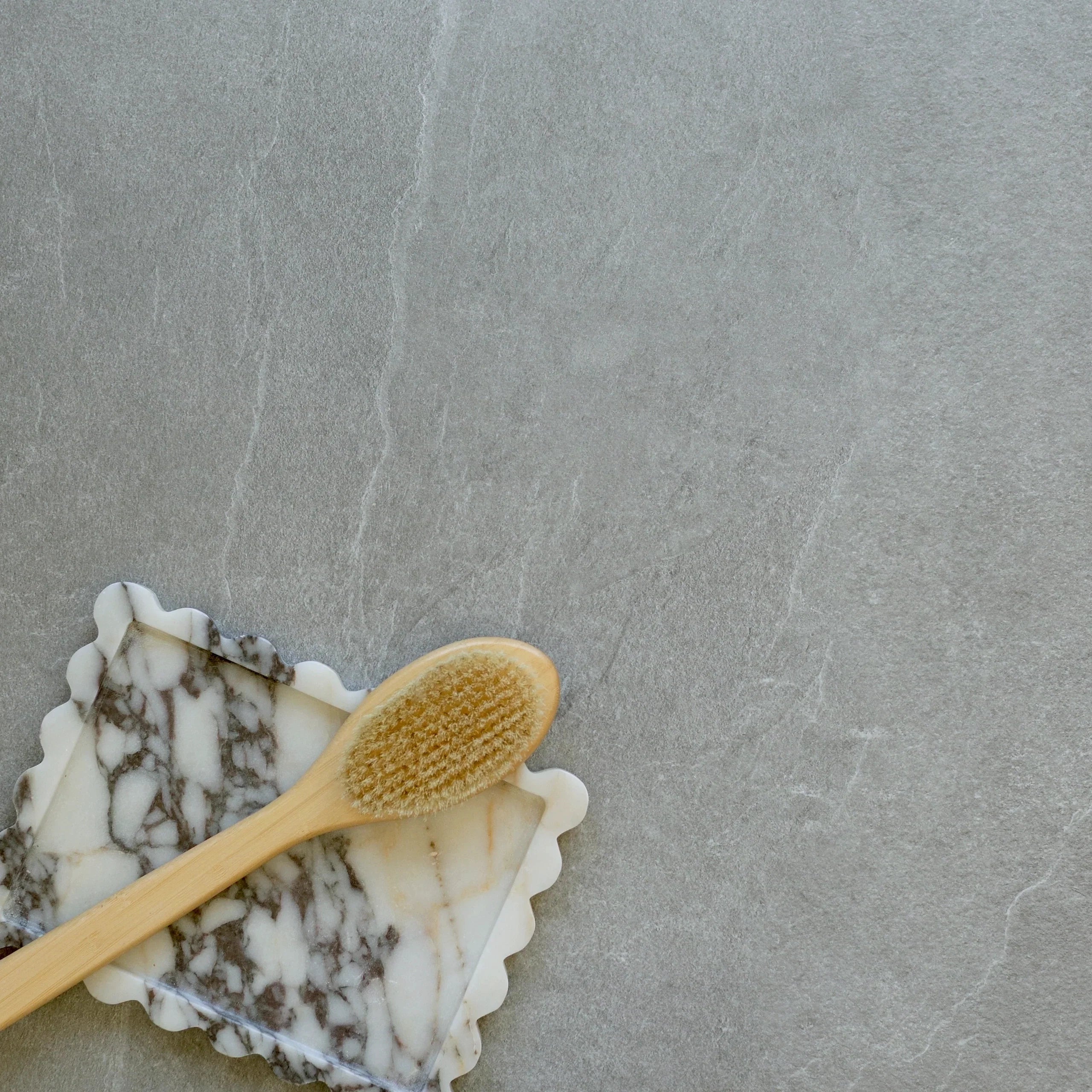 Smooth gray porcelain tile surface with subtle veining alongside a wooden bath brush resting on a marble soap dish