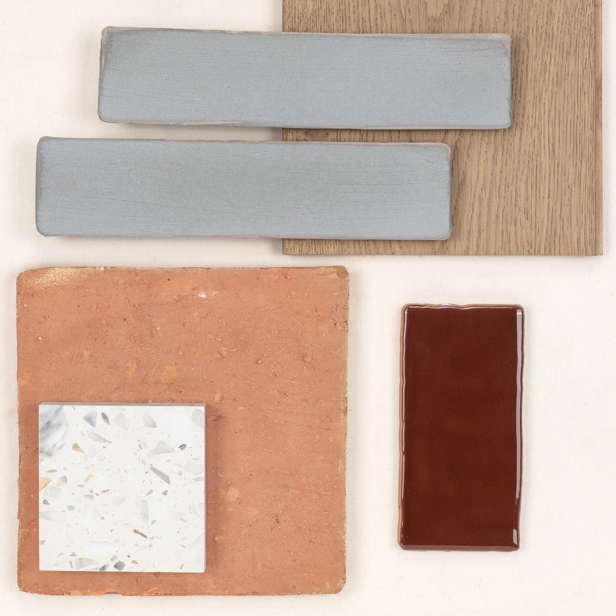 Arrangement of terracotta, glossy brown, pale blue ceramic tiles, terrazzo sample, and natural oak wood on a light surface