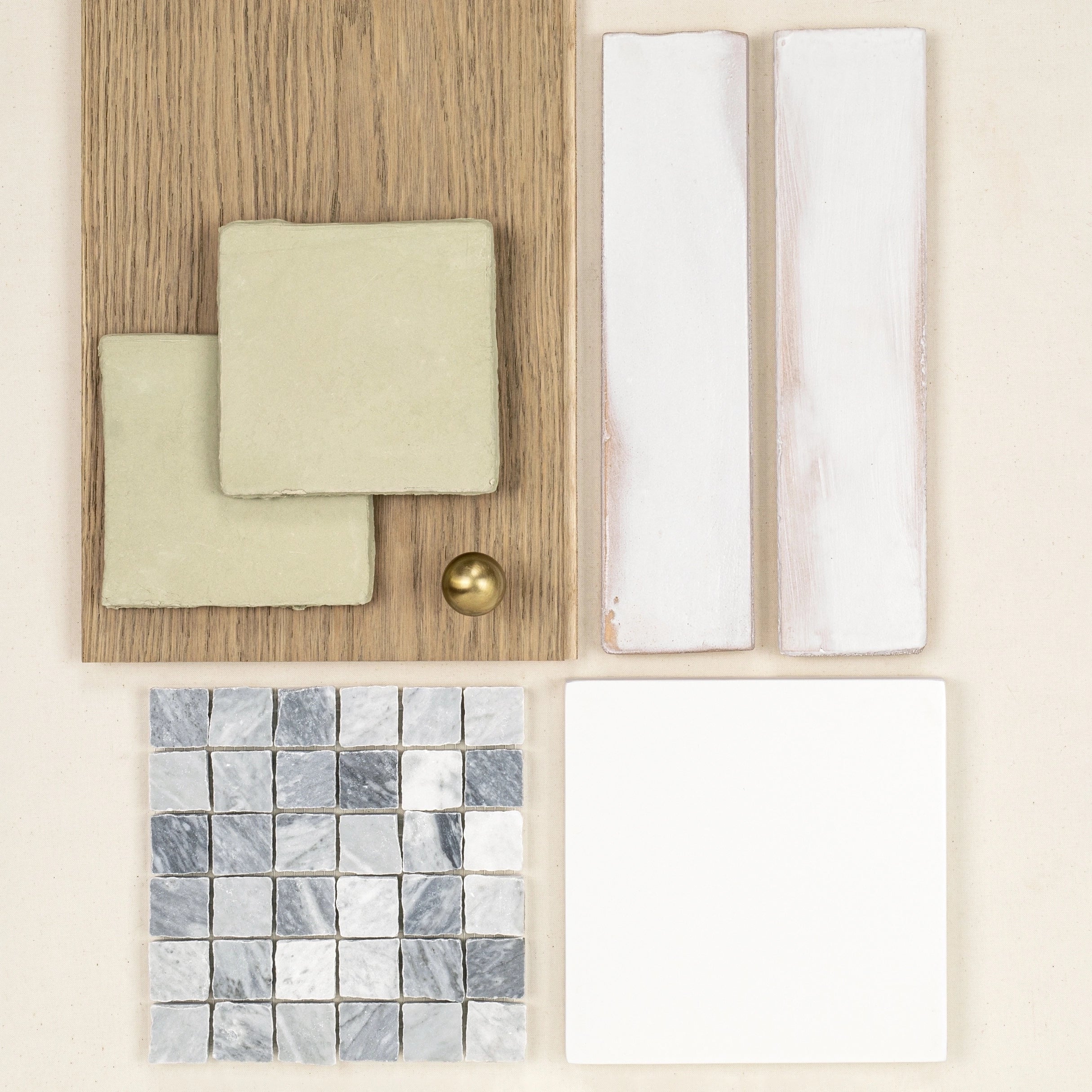 Collection of ceramic and marble tile samples in soft greens, whites, and grays arranged with oak wood and a brass knob on pale background