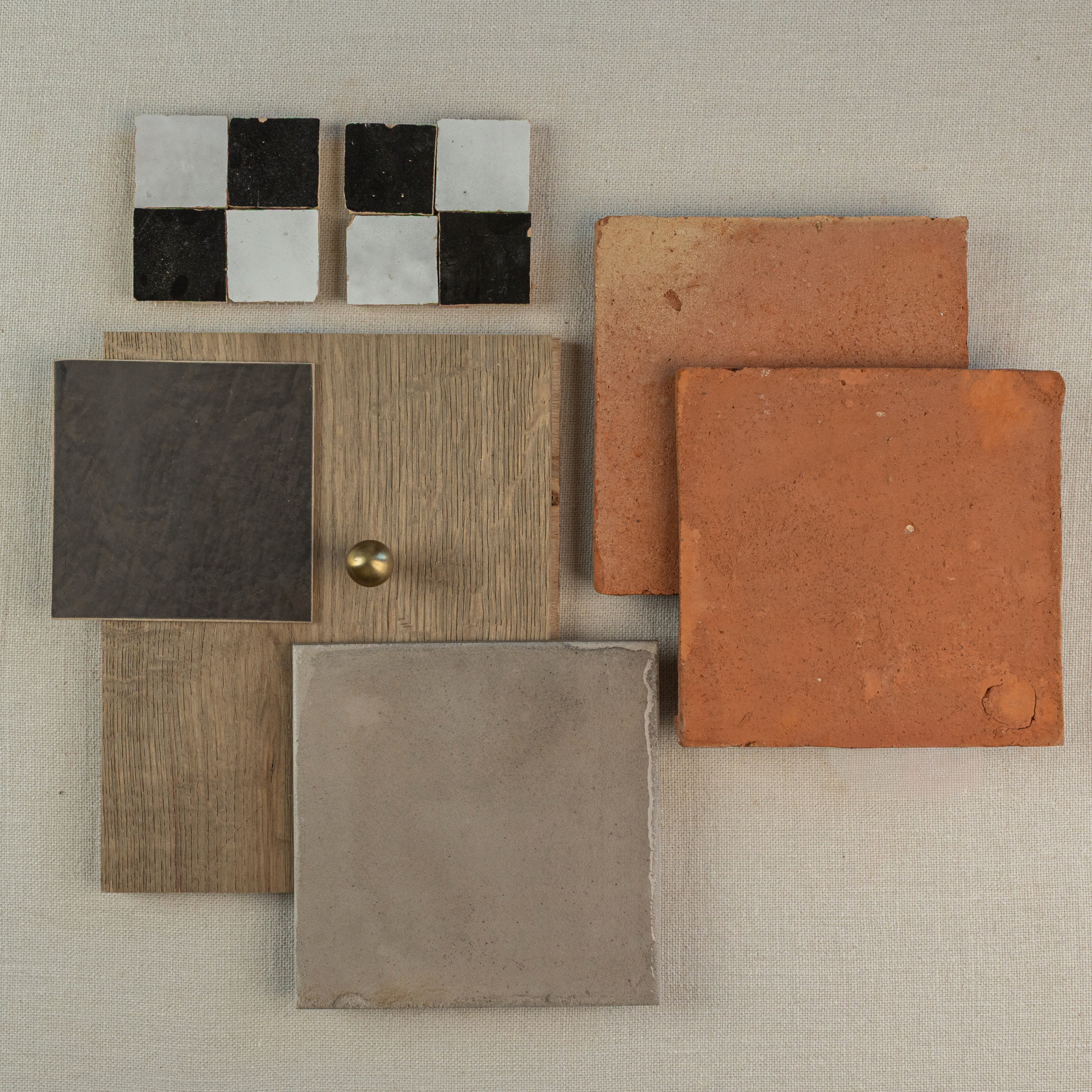 Assortment of handmade terracotta and ceramic tiles with wood and metal samples on neutral fabric background