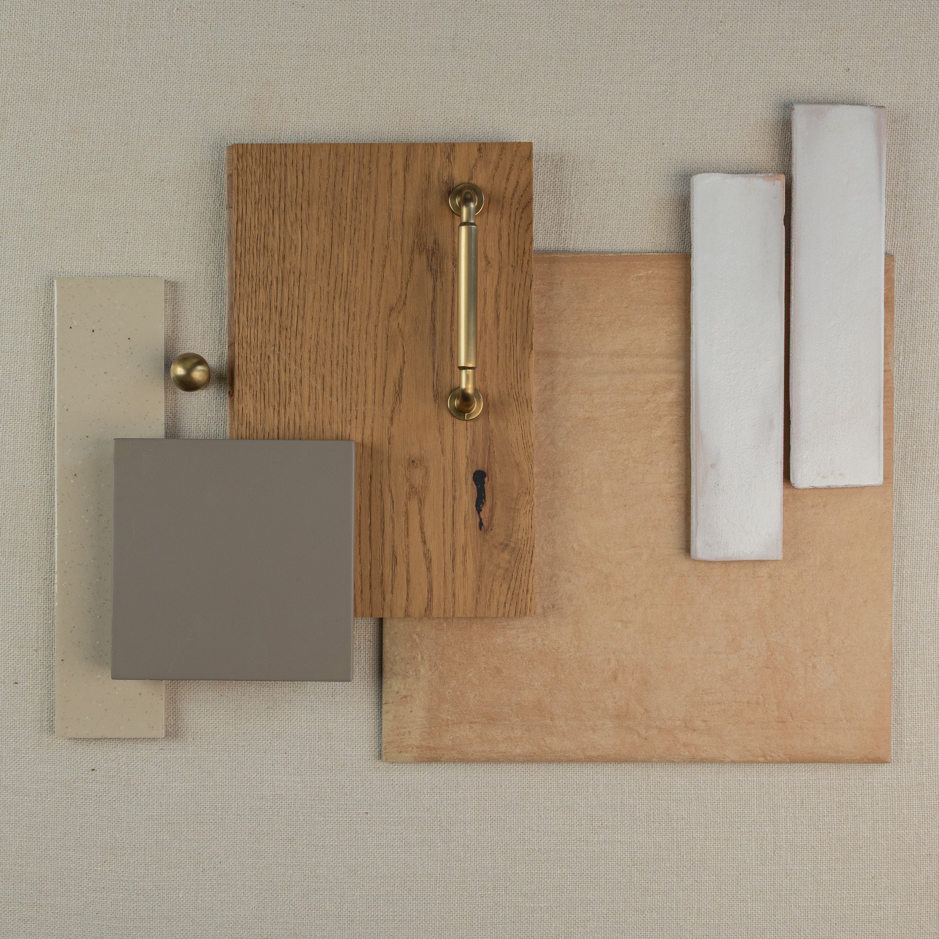 Arrangement of natural wood panel with brass handle, matte gray tile, beige and white ceramic tiles on neutral fabric surface